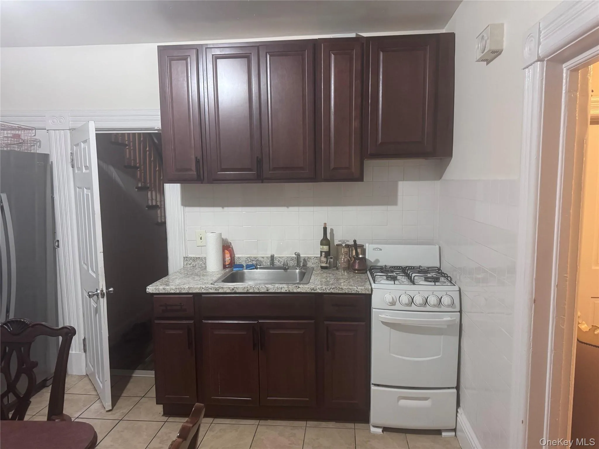 Kitchen with white gas range oven, dark brown cabinets, light tile patterned flooring, and decorative backsplash Kitchen with white gas range oven, dark brown cabinets, light tile patterned flooring, and decorative backsplash