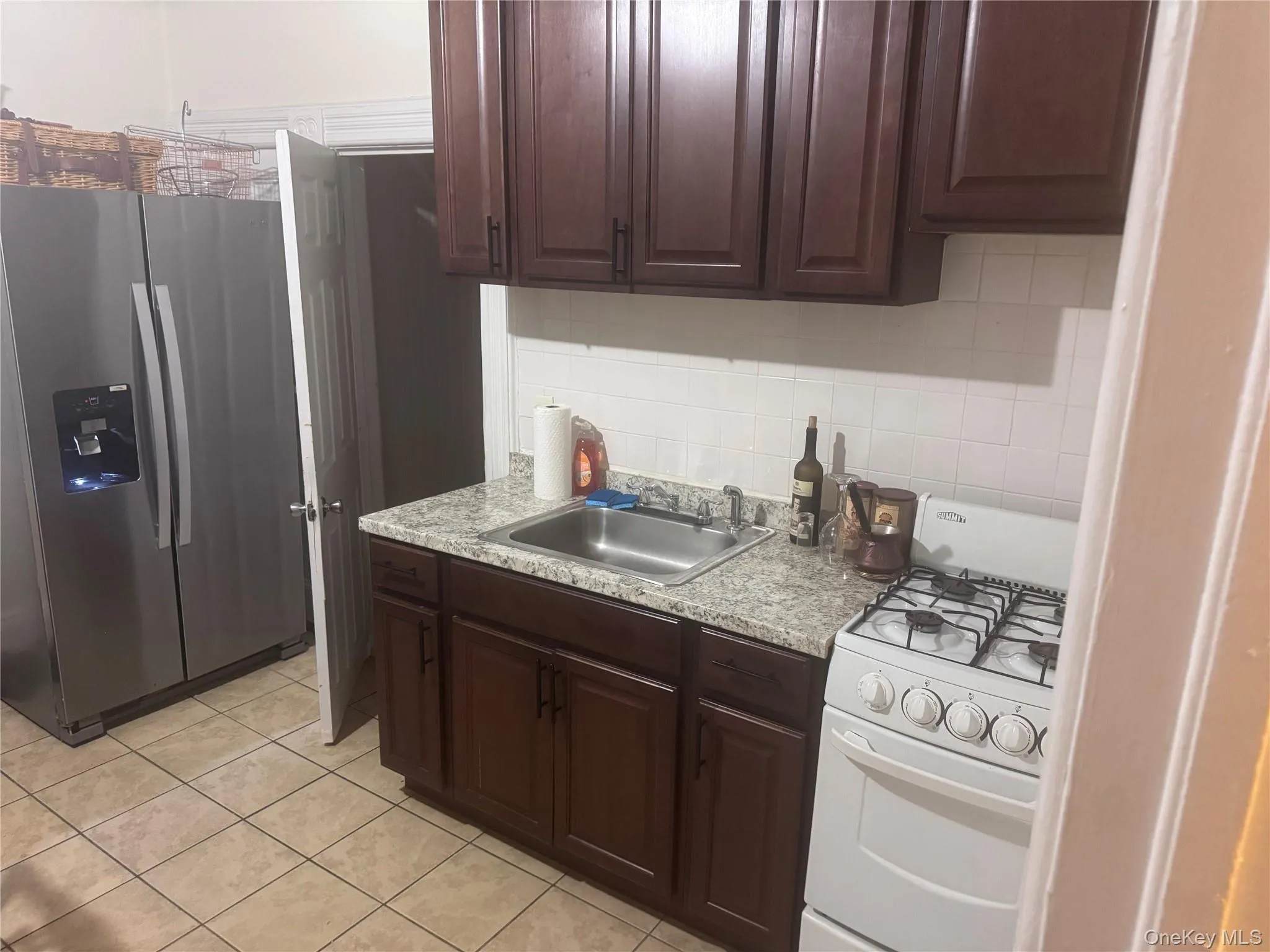 Kitchen featuring stainless steel fridge with ice dispenser, white gas range oven, dark brown cabinets, light countertops, and backsplash Kitchen featuring stainless steel fridge with ice dispenser, white gas range oven, dark brown cabinets, light countertops, and backsplash
