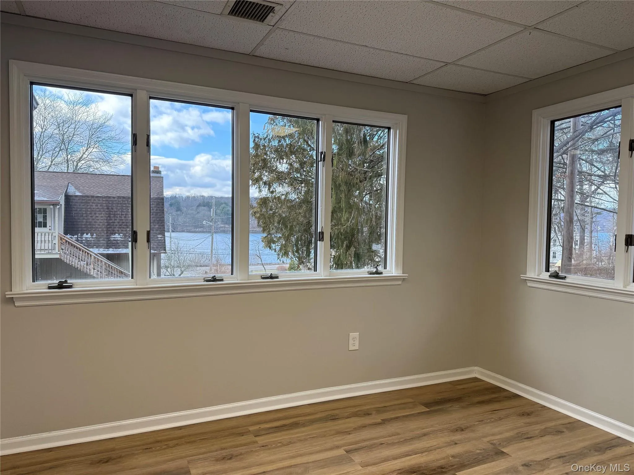 Empty room featuring wood finished floors, a drop ceiling, healthy amount of natural light, and a water view Empty room featuring wood finished floors, a drop ceiling, healthy amount of natural light, and a water view