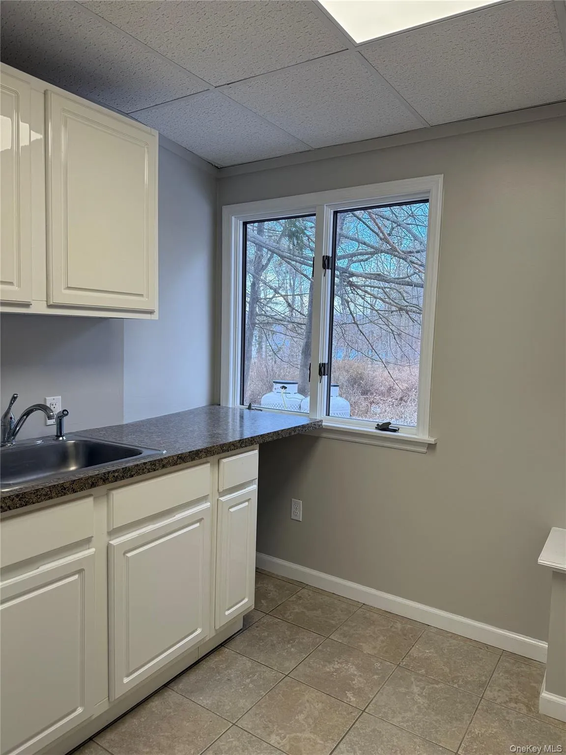 Kitchen featuring dark countertops, white cabinets, a drop ceiling, and light tile patterned floors Kitchen featuring dark countertops, white cabinets, a drop ceiling, and light tile patterned floors