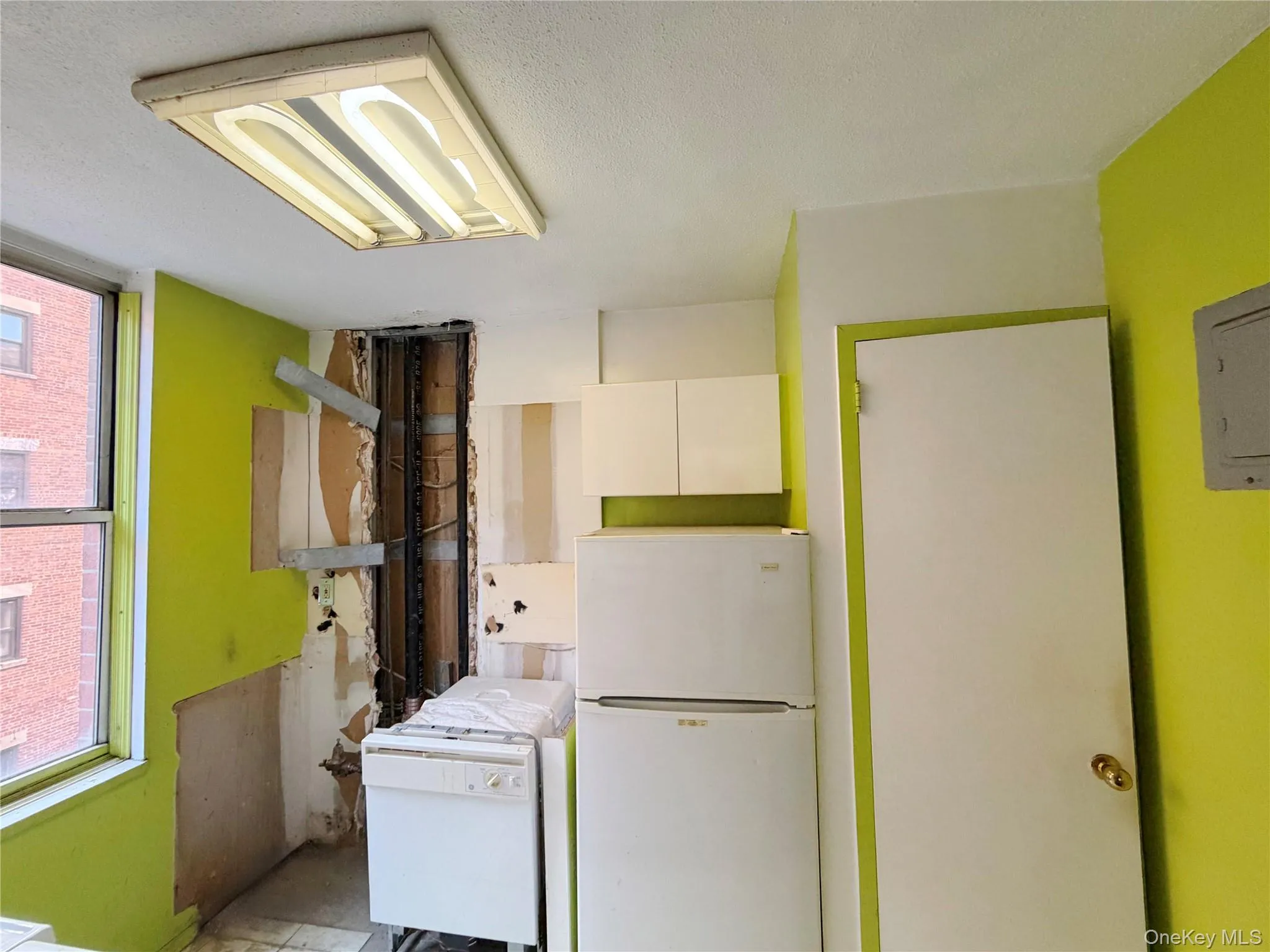 Kitchen with freestanding refrigerator, white cabinetry, a textured ceiling, and electric panel Kitchen with freestanding refrigerator, white cabinetry, a textured ceiling, and electric panel