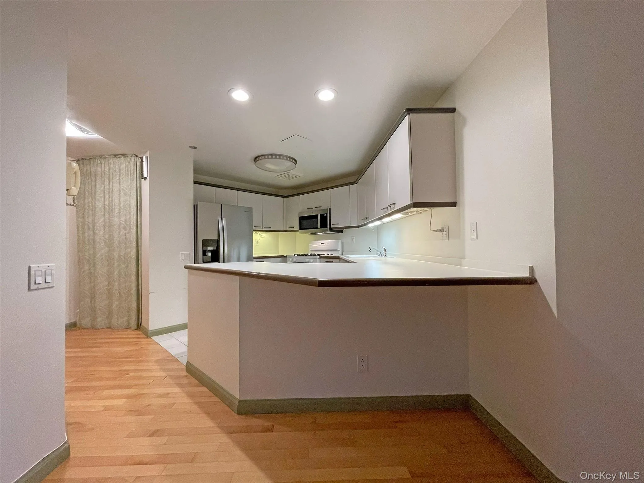 Kitchen featuring a peninsula, light countertops, white cabinetry, appliances with stainless steel finishes, and light wood finished floors Kitchen featuring a peninsula, light countertops, white cabinetry, appliances with stainless steel finishes, and light wood finished floors