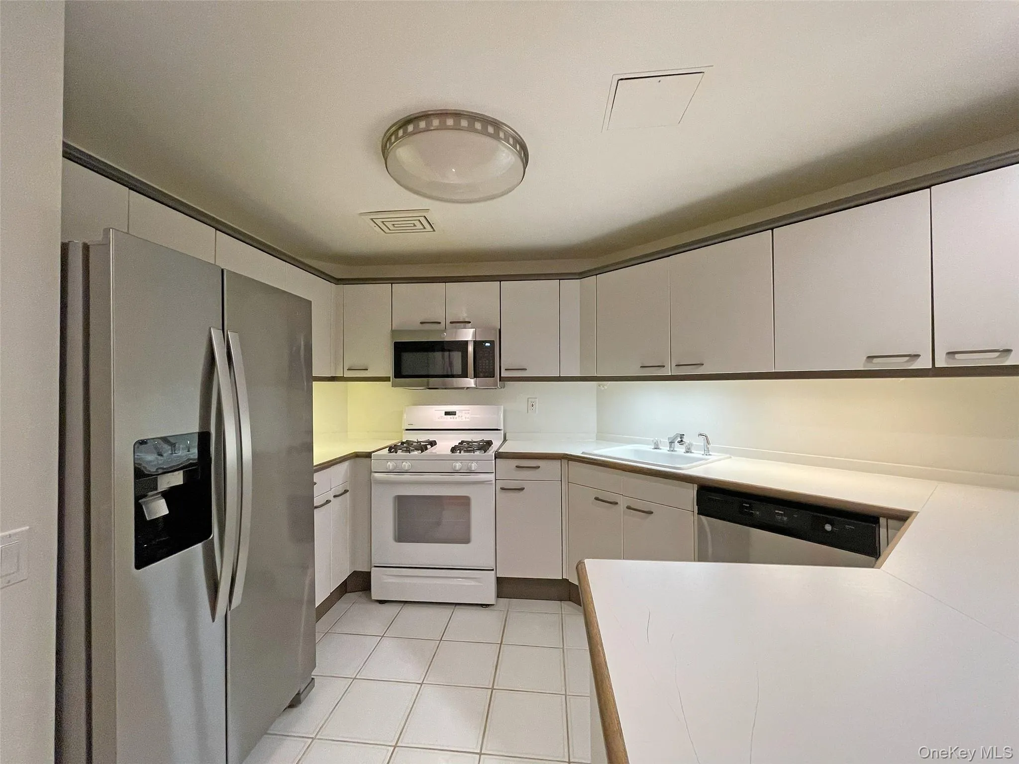 Kitchen featuring appliances with stainless steel finishes, light countertops, white cabinets, and light tile patterned flooring Kitchen featuring appliances with stainless steel finishes, light countertops, white cabinets, and light tile patterned flooring