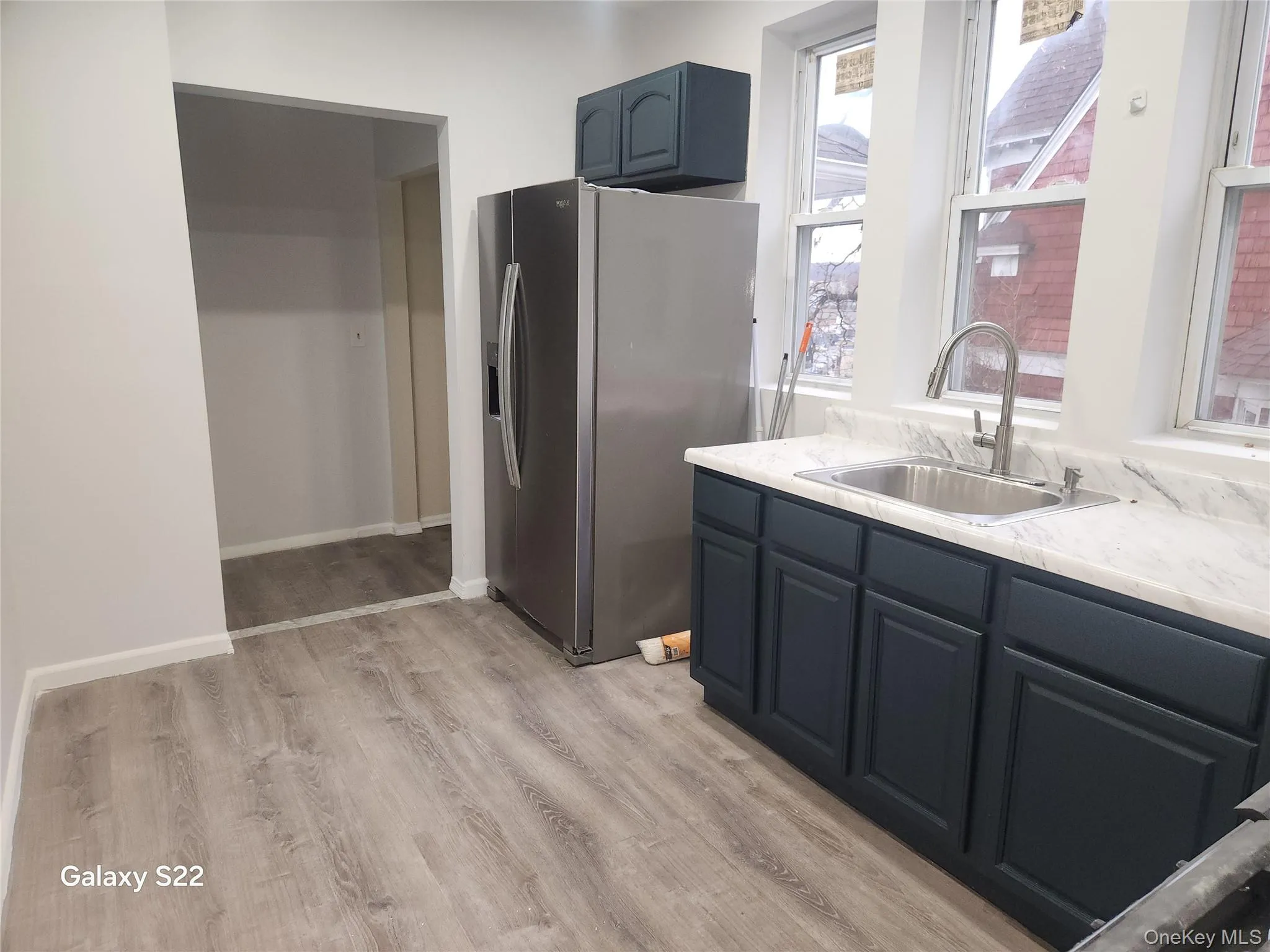 Kitchen with stainless steel refrigerator with ice dispenser, light countertops, light wood finished floors, and blue cabinetry Kitchen with stainless steel refrigerator with ice dispenser, light countertops, light wood finished floors, and blue cabinetry