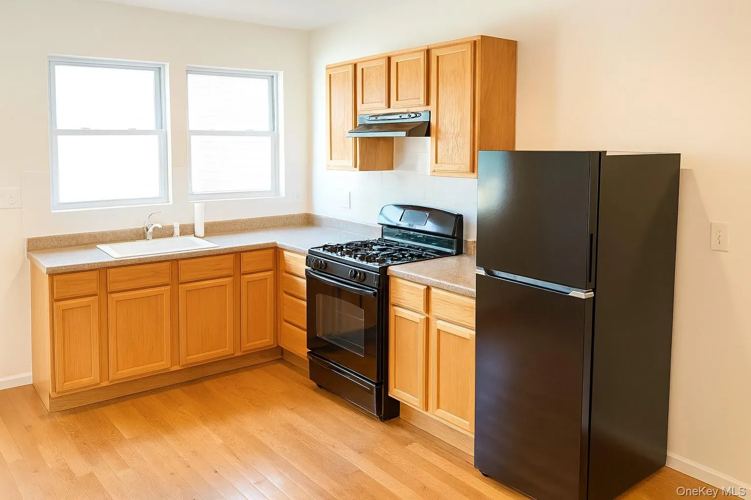 Kitchen featuring black appliances, light countertops, light wood-type flooring, and under cabinet range hood Kitchen featuring black appliances, light countertops, light wood-type flooring, and under cabinet range hood