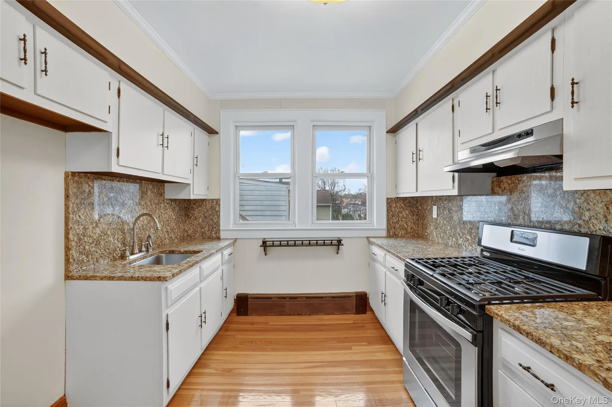 Kitchen with stainless steel gas range oven, light stone counters, white cabinetry, under cabinet range hood, and crown molding Kitchen with stainless steel gas range oven, light stone counters, white cabinetry, under cabinet range hood, and crown molding
