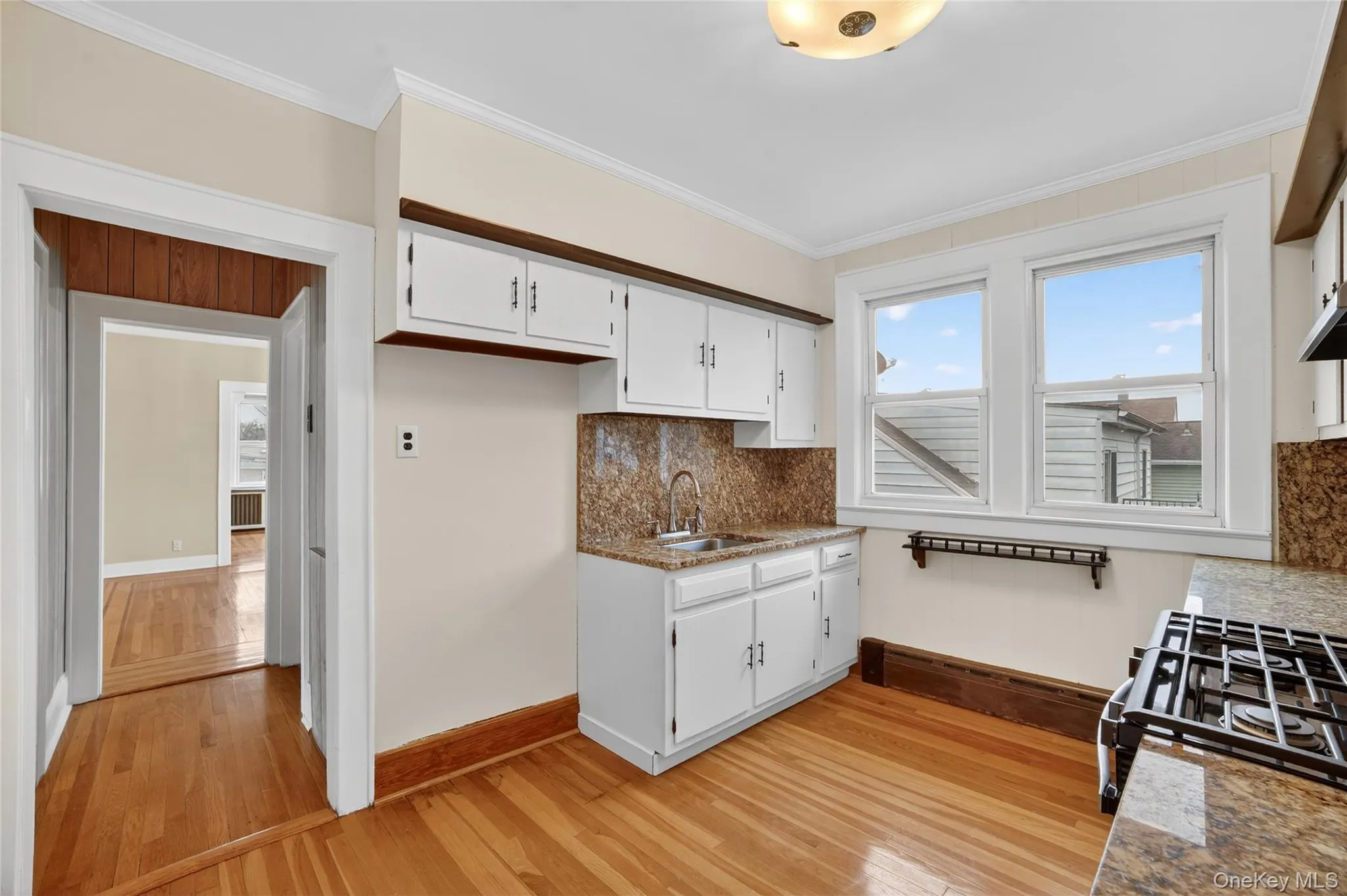 Kitchen featuring dark stone countertops, black gas range oven, ornamental molding, light wood-style flooring, and white cabinets Kitchen featuring dark stone countertops, black gas range oven, ornamental molding, light wood-style flooring, and white cabinets