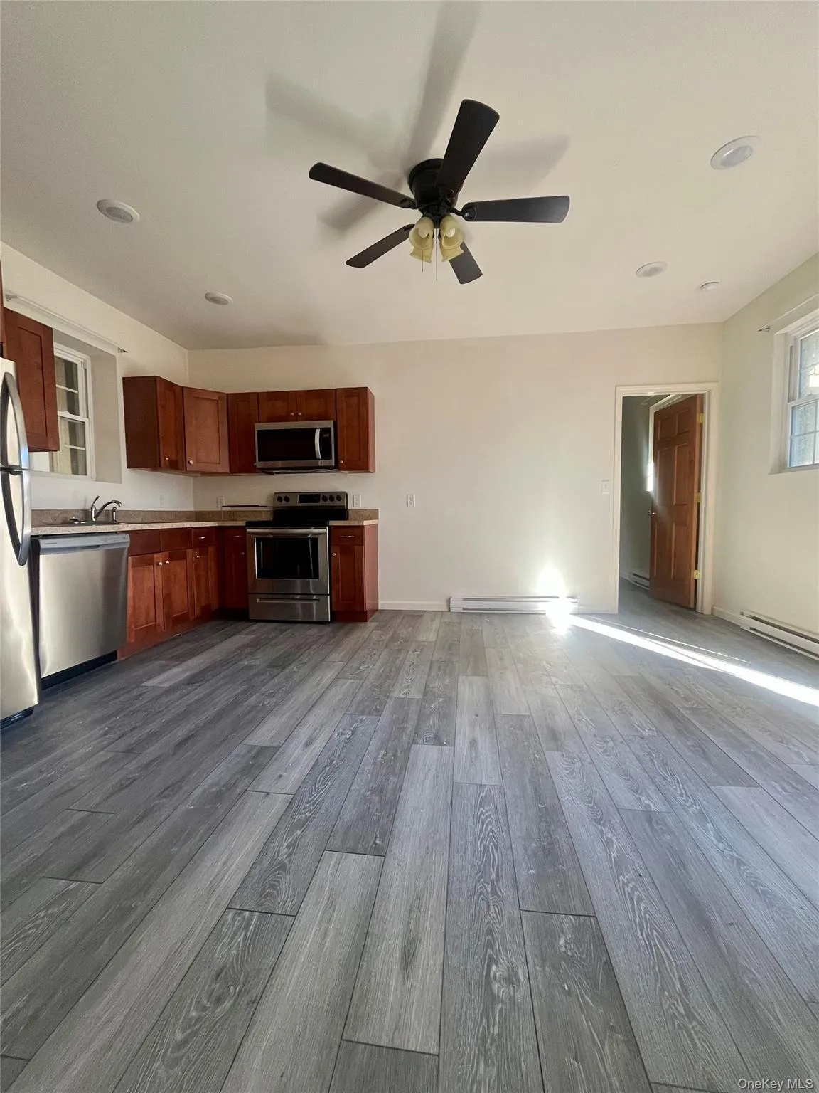 Kitchen featuring stainless steel appliances, baseboard heating, dark wood-type flooring, light countertops, and ceiling fan Kitchen featuring stainless steel appliances, baseboard heating, dark wood-type flooring, light countertops, and ceiling fan
