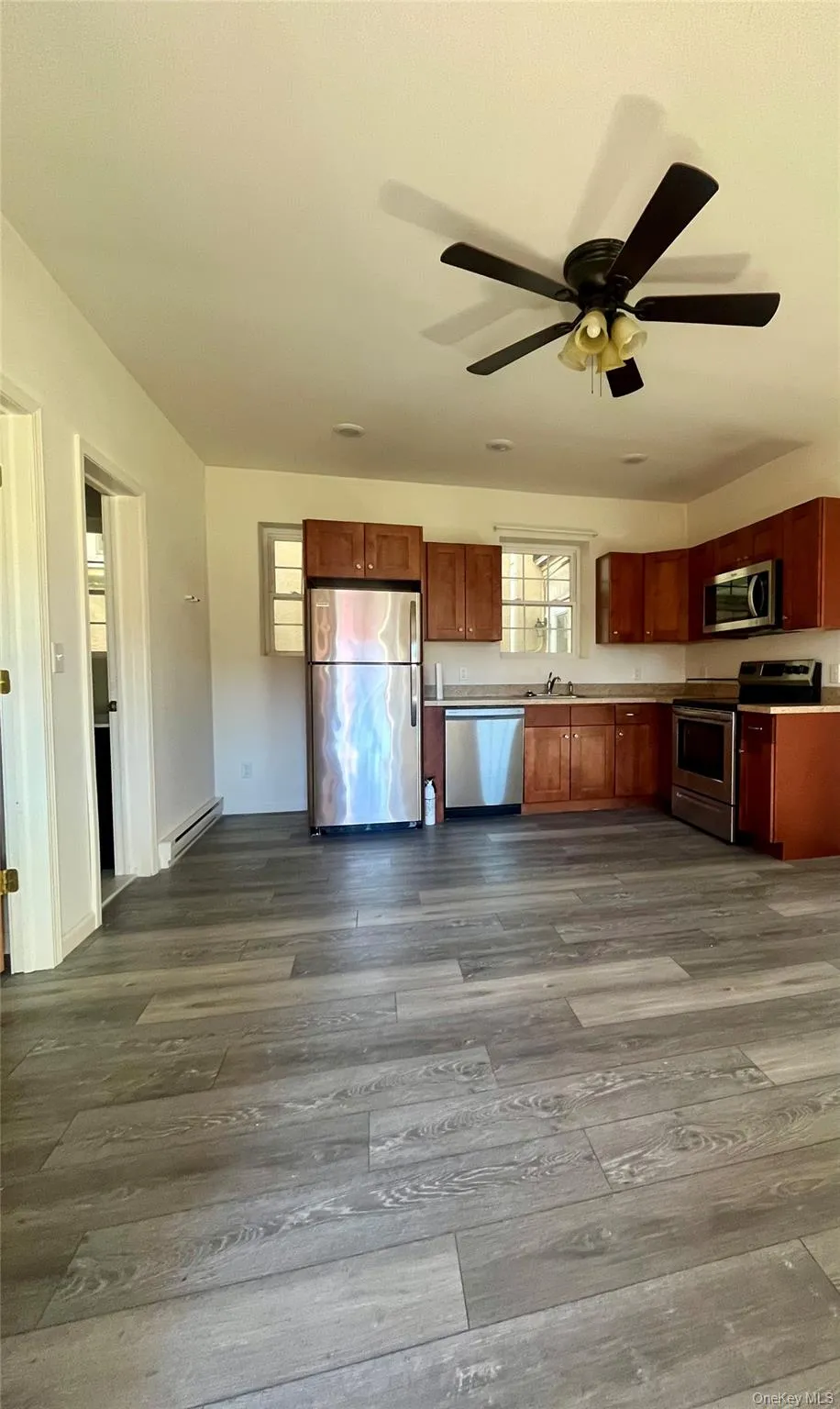 Kitchen with stainless steel appliances, brown cabinets, a baseboard heating unit, and dark wood-type flooring Kitchen with stainless steel appliances, brown cabinets, a baseboard heating unit, and dark wood-type flooring
