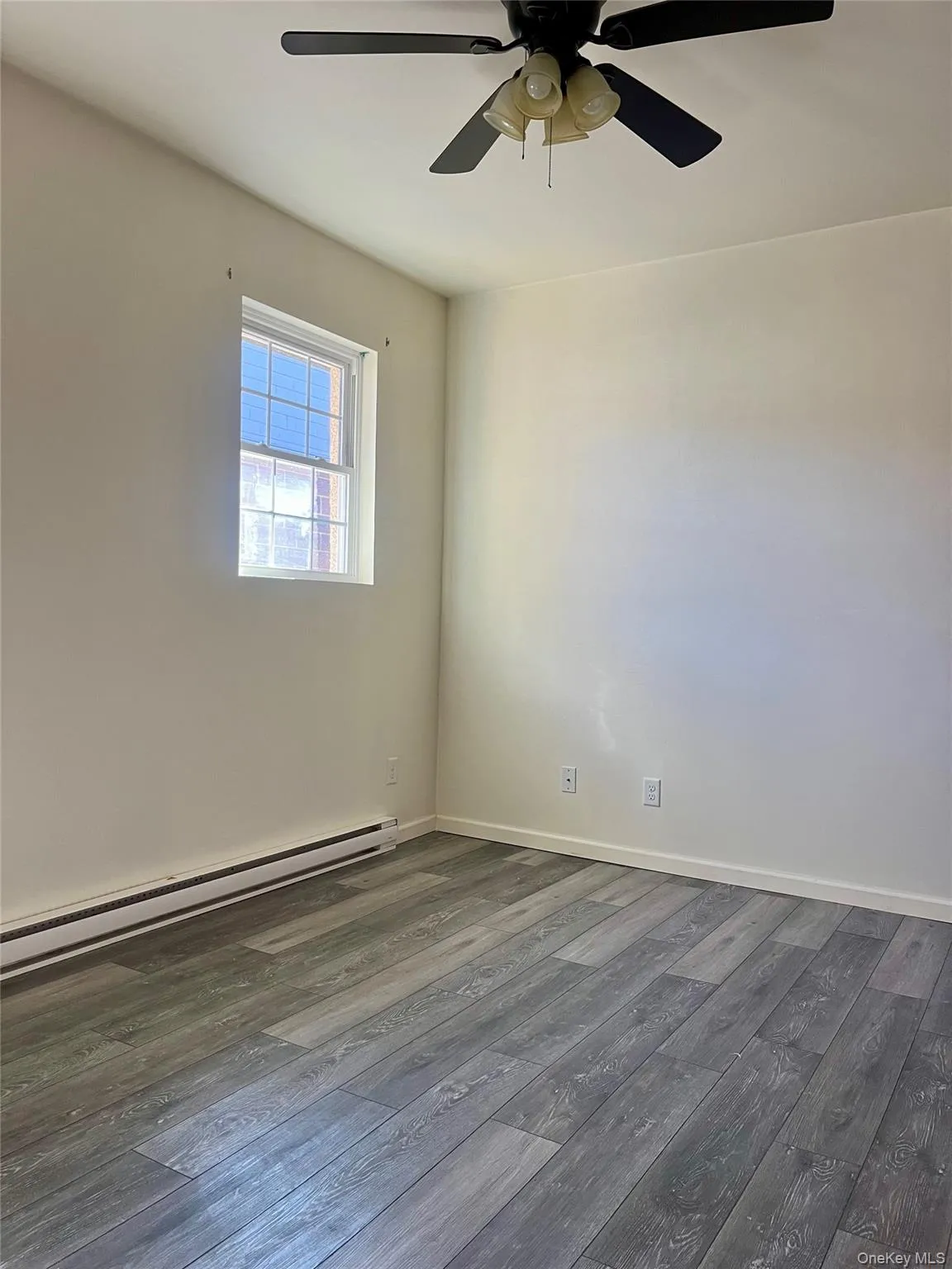 Unfurnished room with baseboard heating, dark wood-style floors, and ceiling fan Unfurnished room with baseboard heating, dark wood-style floors, and ceiling fan