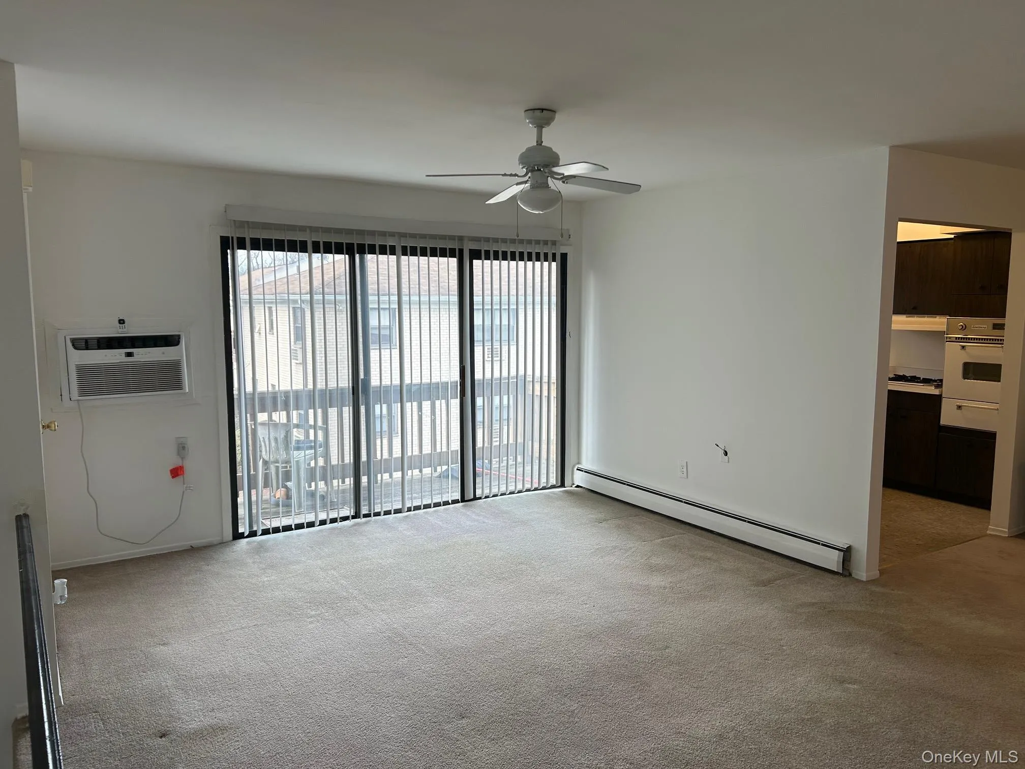 Unfurnished room featuring baseboard heating, light carpet, a wall mounted air conditioner, and ceiling fan Unfurnished room featuring baseboard heating, light carpet, a wall mounted air conditioner, and ceiling fan