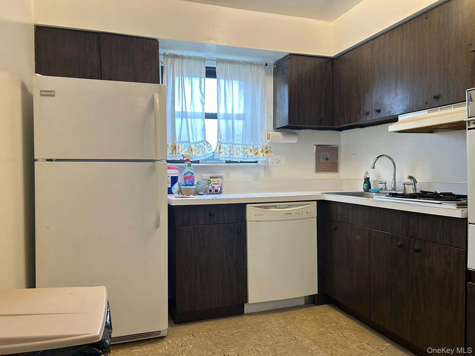 Kitchen featuring dark brown cabinetry, white appliances, light countertops, under cabinet range hood, and light flooring Kitchen featuring dark brown cabinetry, white appliances, light countertops, under cabinet range hood, and light flooring