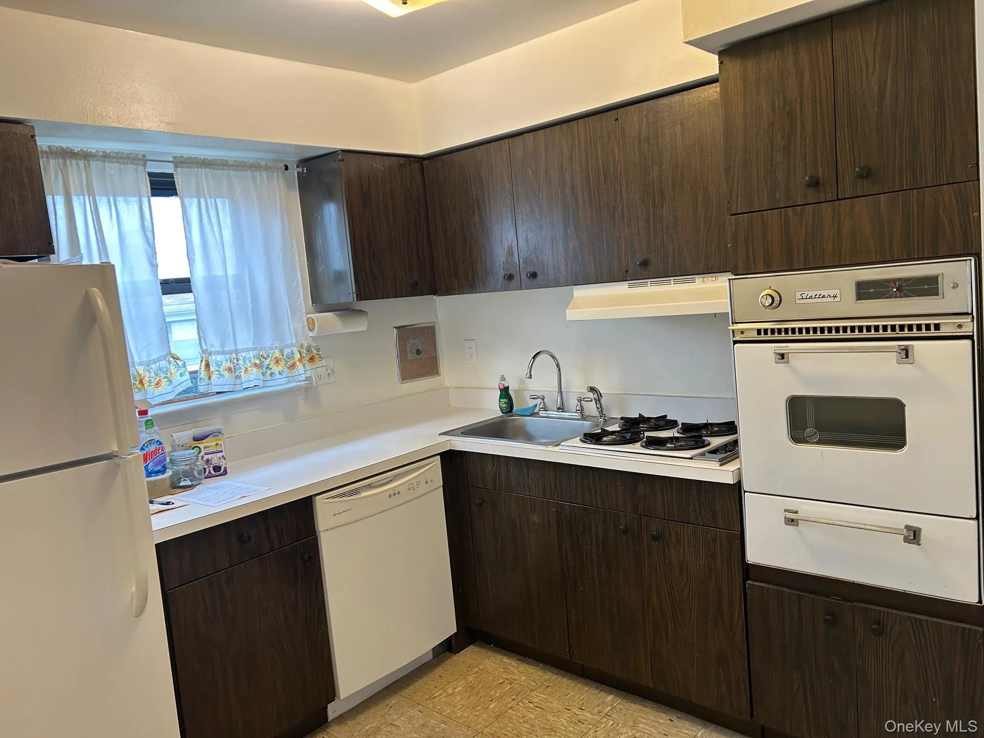 Kitchen featuring dark brown cabinets, white appliances, light countertops, and a warming drawer Kitchen featuring dark brown cabinets, white appliances, light countertops, and a warming drawer