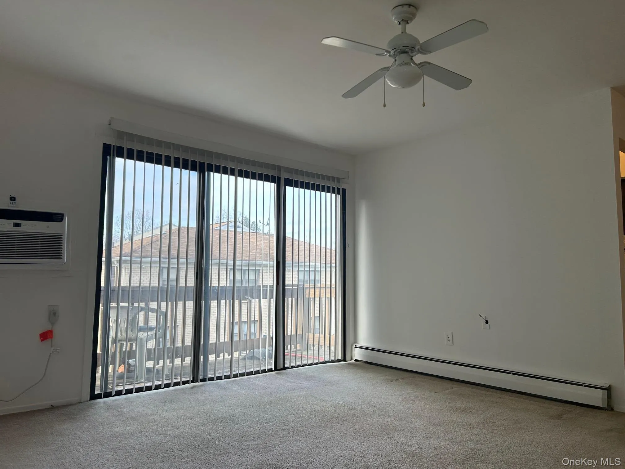 Spare room featuring a baseboard radiator, plenty of natural light, a wall mounted air conditioner, and light colored carpet Spare room featuring a baseboard radiator, plenty of natural light, a wall mounted air conditioner, and light colored carpet
