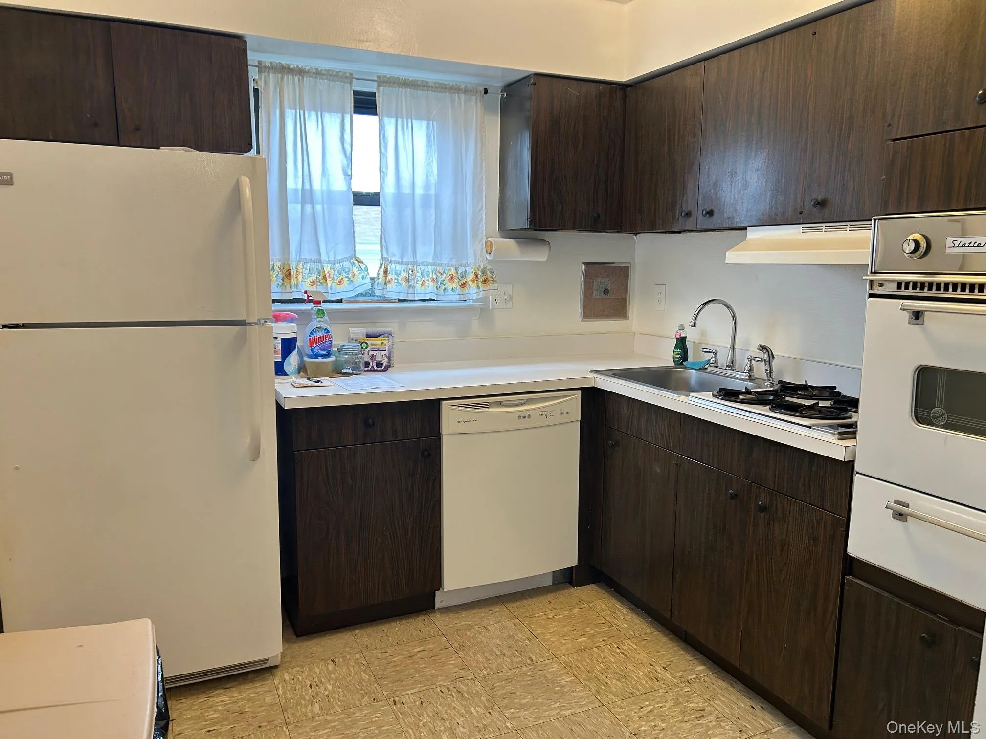 Kitchen featuring white appliances, dark brown cabinets, light countertops, a warming drawer, and under cabinet range hood Kitchen featuring white appliances, dark brown cabinets, light countertops, a warming drawer, and under cabinet range hood