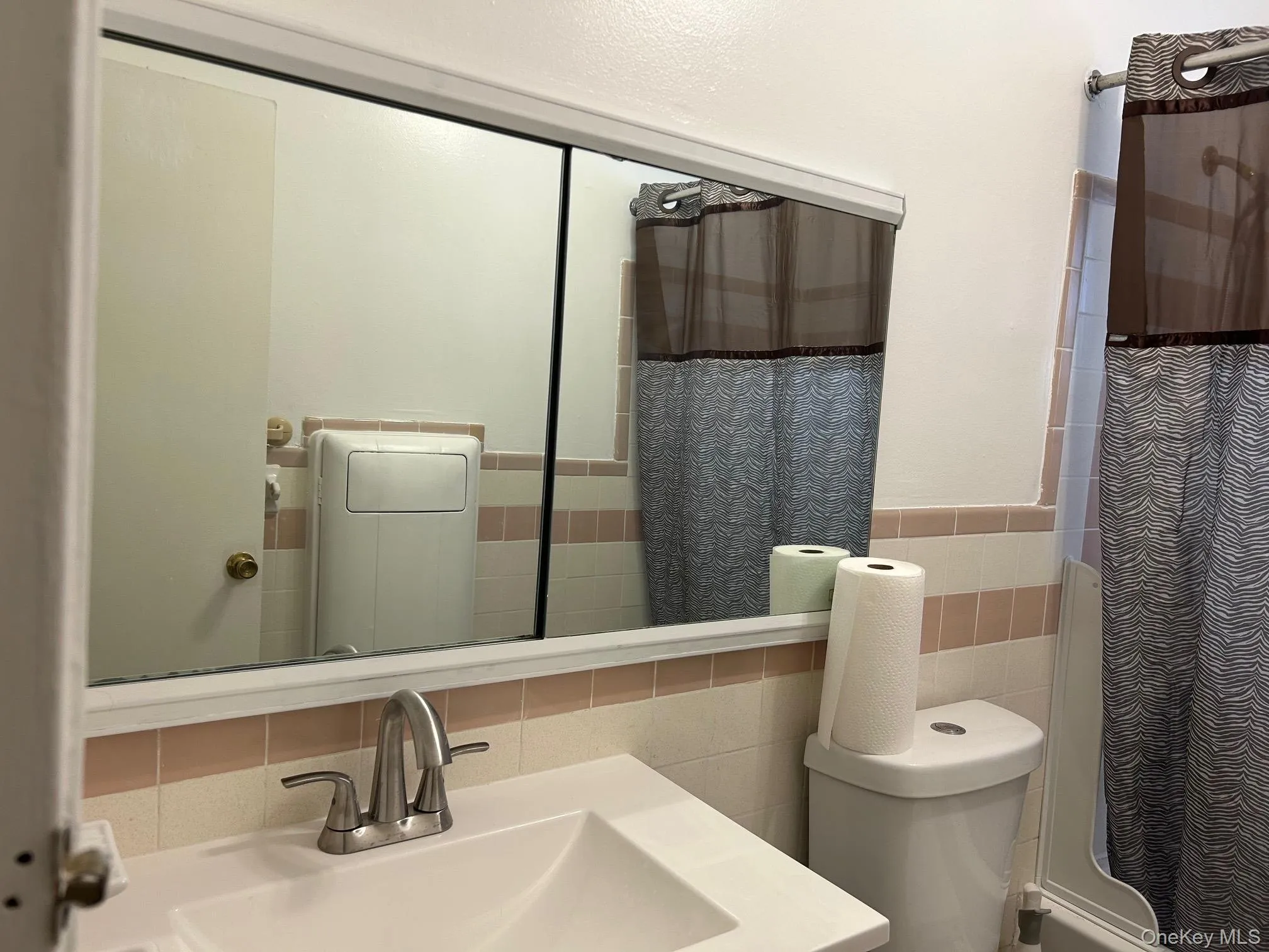 Full bathroom with tile walls, vanity, a wainscoted wall, and shower / tub combo Full bathroom with tile walls, vanity, a wainscoted wall, and shower / tub combo