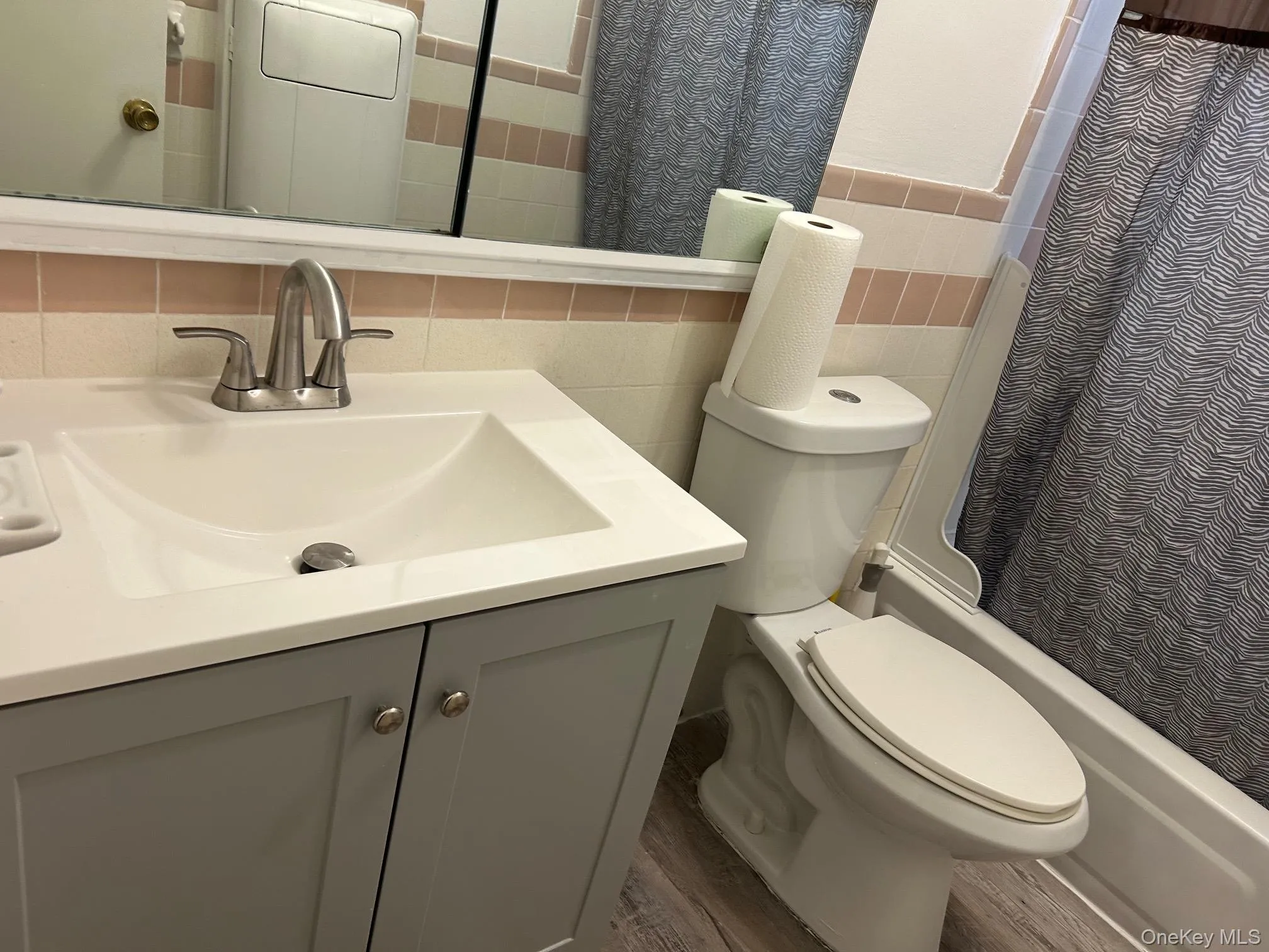 Bathroom with tile walls, vanity, shower / bath combination with curtain, and dark wood-style floors Bathroom with tile walls, vanity, shower / bath combination with curtain, and dark wood-style floors
