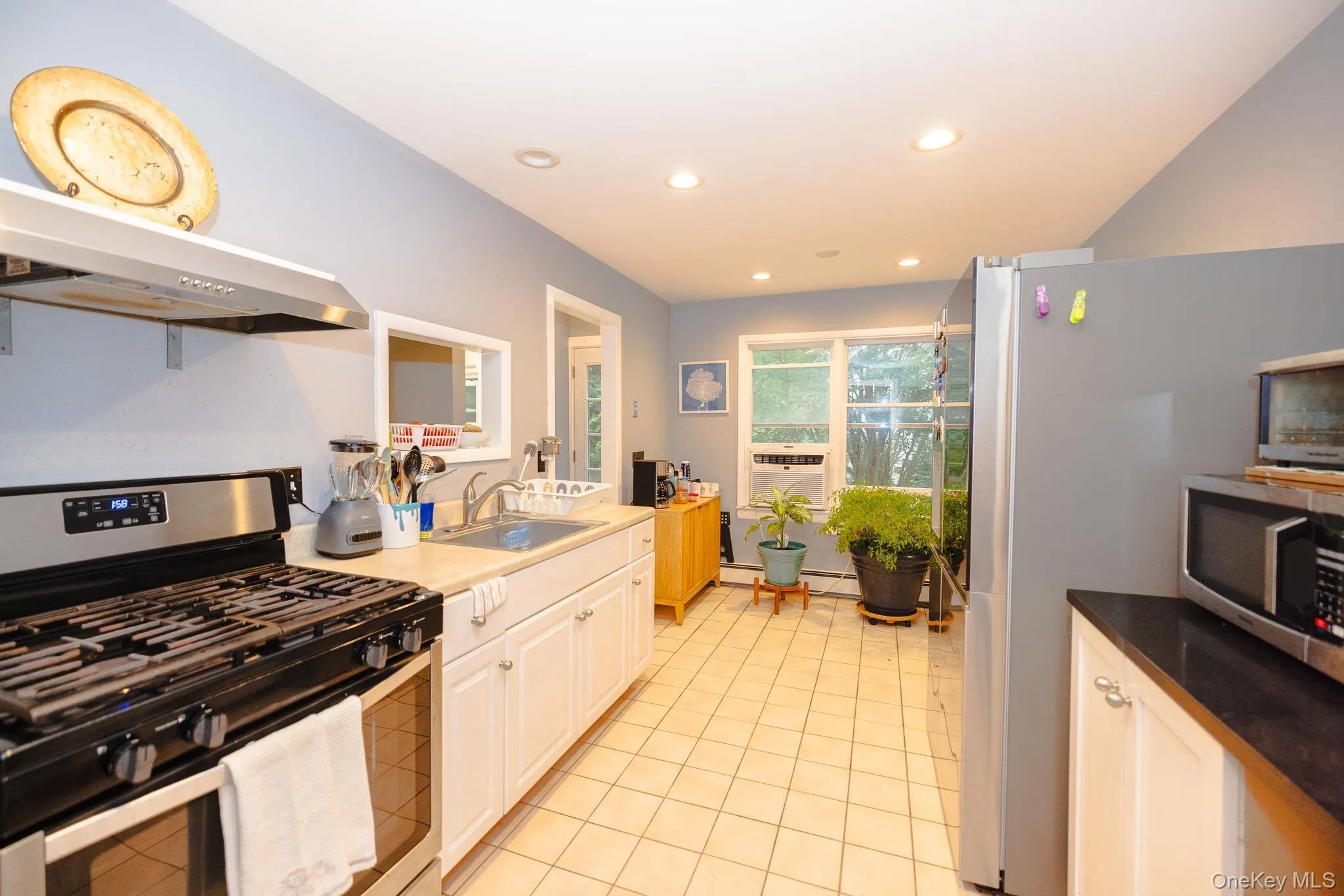 Kitchen with appliances with stainless steel finishes, under cabinet range hood, recessed lighting, light tile patterned floors, and white cabinetry Kitchen with appliances with stainless steel finishes, under cabinet range hood, recessed lighting, light tile patterned floors, and white cabinetry