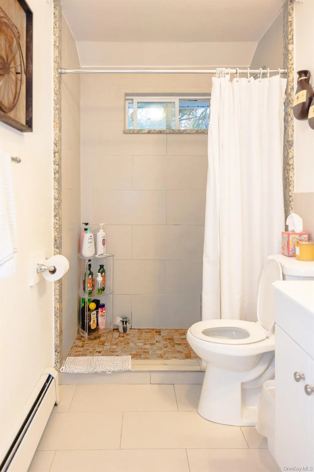 Bathroom with a baseboard heating unit, vanity, tiled shower, and tile patterned flooring Bathroom with a baseboard heating unit, vanity, tiled shower, and tile patterned flooring