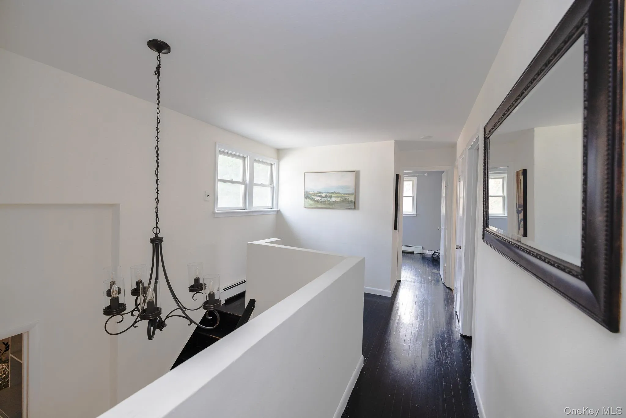 Hall with dark wood finished floors, a chandelier, baseboard heating, and an upstairs landing Hall with dark wood finished floors, a chandelier, baseboard heating, and an upstairs landing