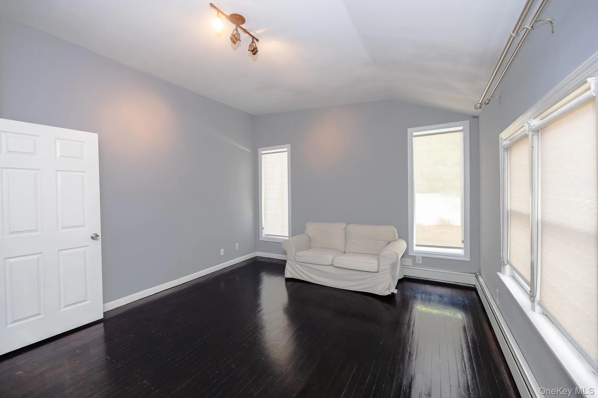 Unfurnished room featuring a baseboard radiator, vaulted ceiling, dark wood-style floors, and healthy amount of natural light Unfurnished room featuring a baseboard radiator, vaulted ceiling, dark wood-style floors, and healthy amount of natural light