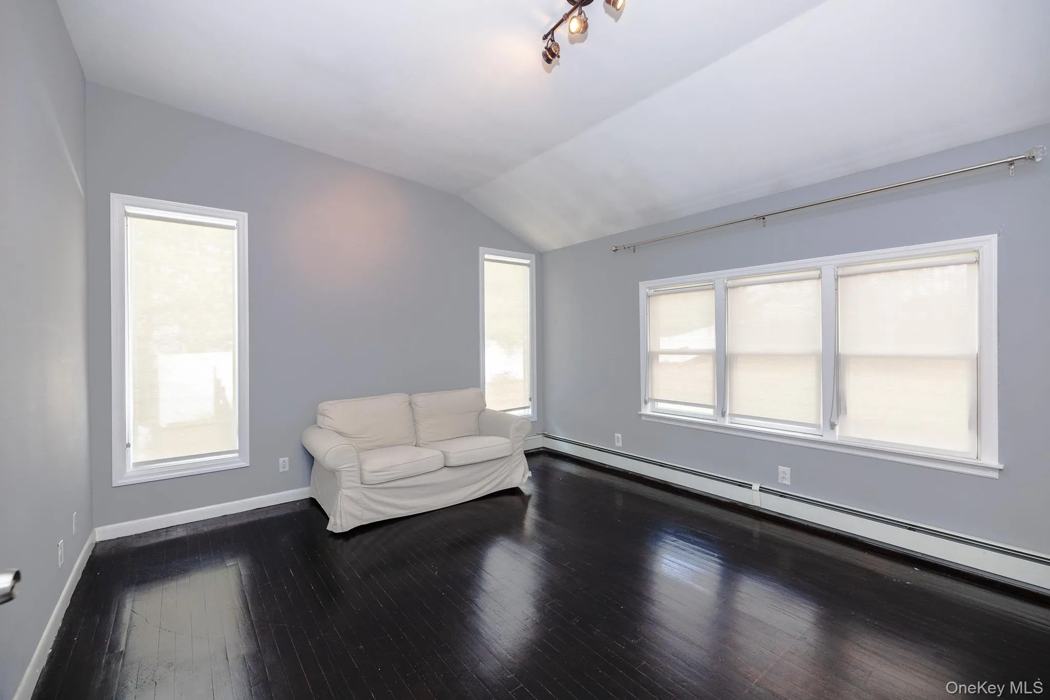 Unfurnished room with a baseboard radiator, vaulted ceiling, and dark wood-type flooring Unfurnished room with a baseboard radiator, vaulted ceiling, and dark wood-type flooring