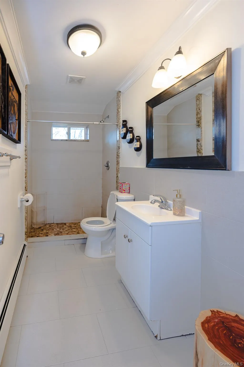 Full bath with a baseboard radiator, vanity, a shower stall, tile walls, and light tile patterned floors Full bath with a baseboard radiator, vanity, a shower stall, tile walls, and light tile patterned floors