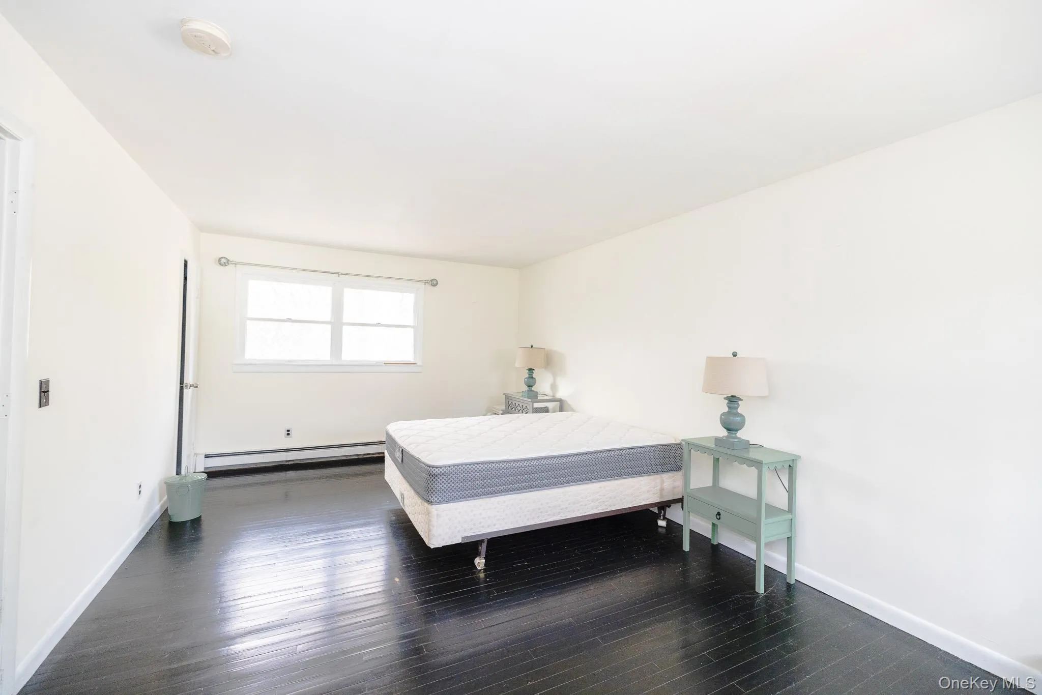 Bedroom featuring dark wood-type flooring and a baseboard radiator Bedroom featuring dark wood-type flooring and a baseboard radiator