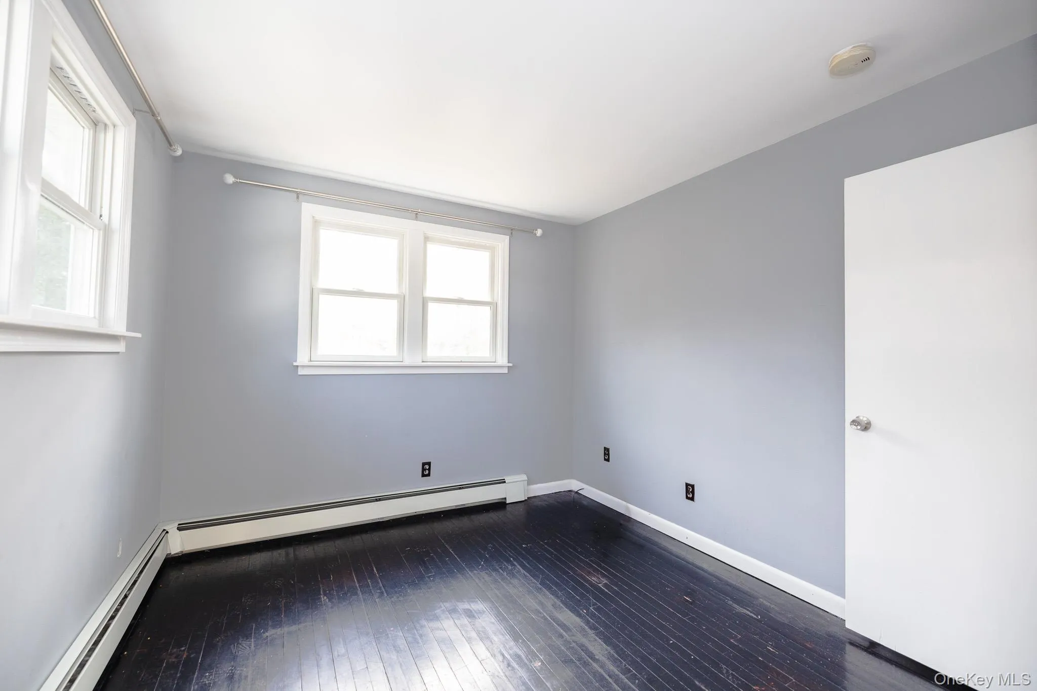 Spare room with healthy amount of natural light, dark wood-style floors, and a baseboard heating unit Spare room with healthy amount of natural light, dark wood-style floors, and a baseboard heating unit