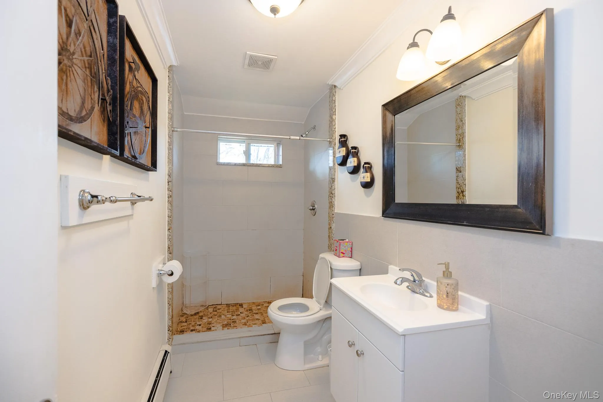 Full bathroom with vanity, a baseboard radiator, light tile patterned floors, a stall shower, and tile walls Full bathroom with vanity, a baseboard radiator, light tile patterned floors, a stall shower, and tile walls