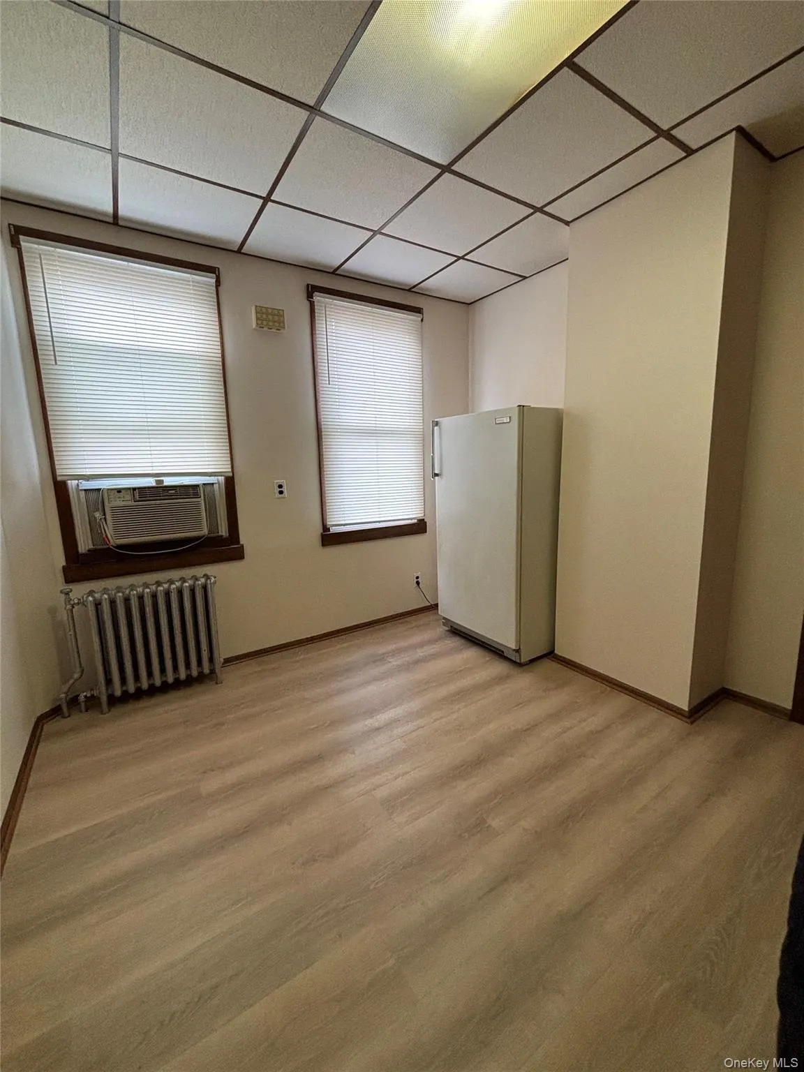 Empty room with a drop ceiling, radiator, light wood-type flooring, and cooling unit Empty room with a drop ceiling, radiator, light wood-type flooring, and cooling unit