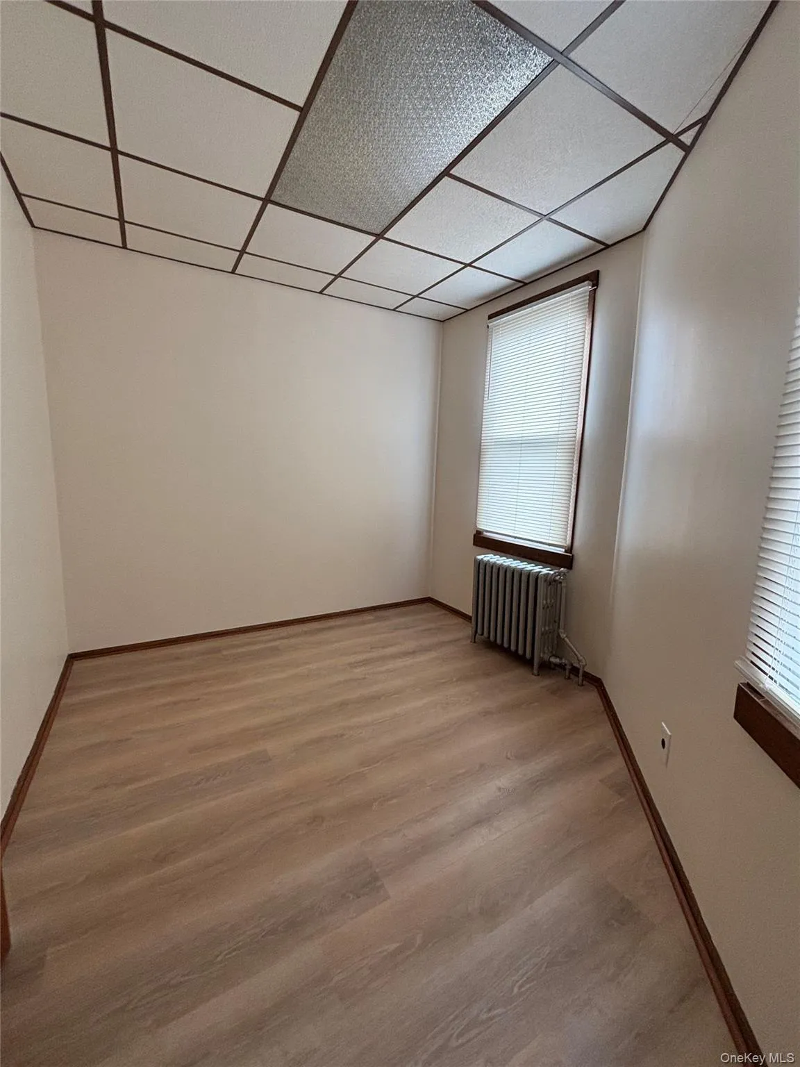 Empty room featuring a drop ceiling, radiator heating unit, and wood finished floors Empty room featuring a drop ceiling, radiator heating unit, and wood finished floors