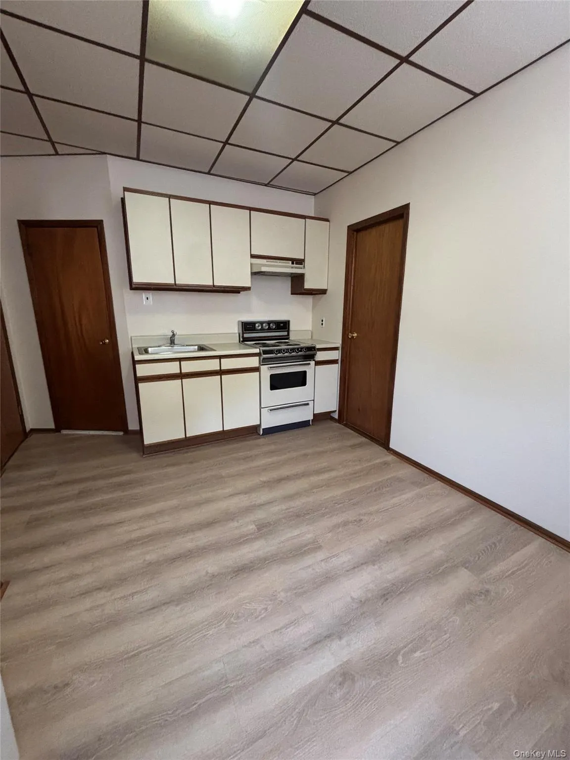 Kitchen featuring white cabinetry, a paneled ceiling, light countertops, white range with electric cooktop, and light wood finished floors Kitchen featuring white cabinetry, a paneled ceiling, light countertops, white range with electric cooktop, and light wood finished floors