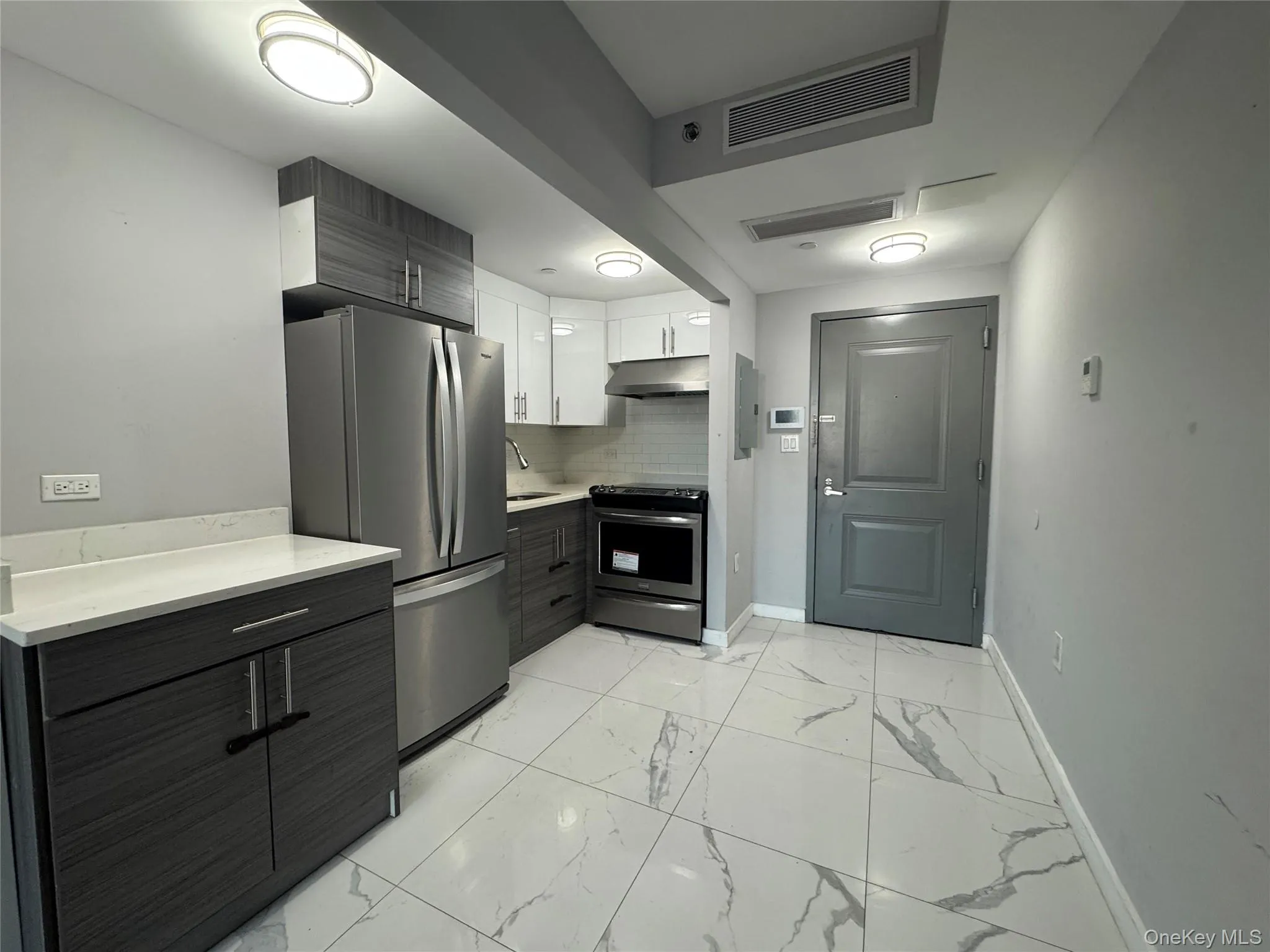 Kitchen featuring stainless steel appliances, modern cabinets, white cabinetry, light marble finish floors, and decorative backsplash Kitchen featuring stainless steel appliances, modern cabinets, white cabinetry, light marble finish floors, and decorative backsplash