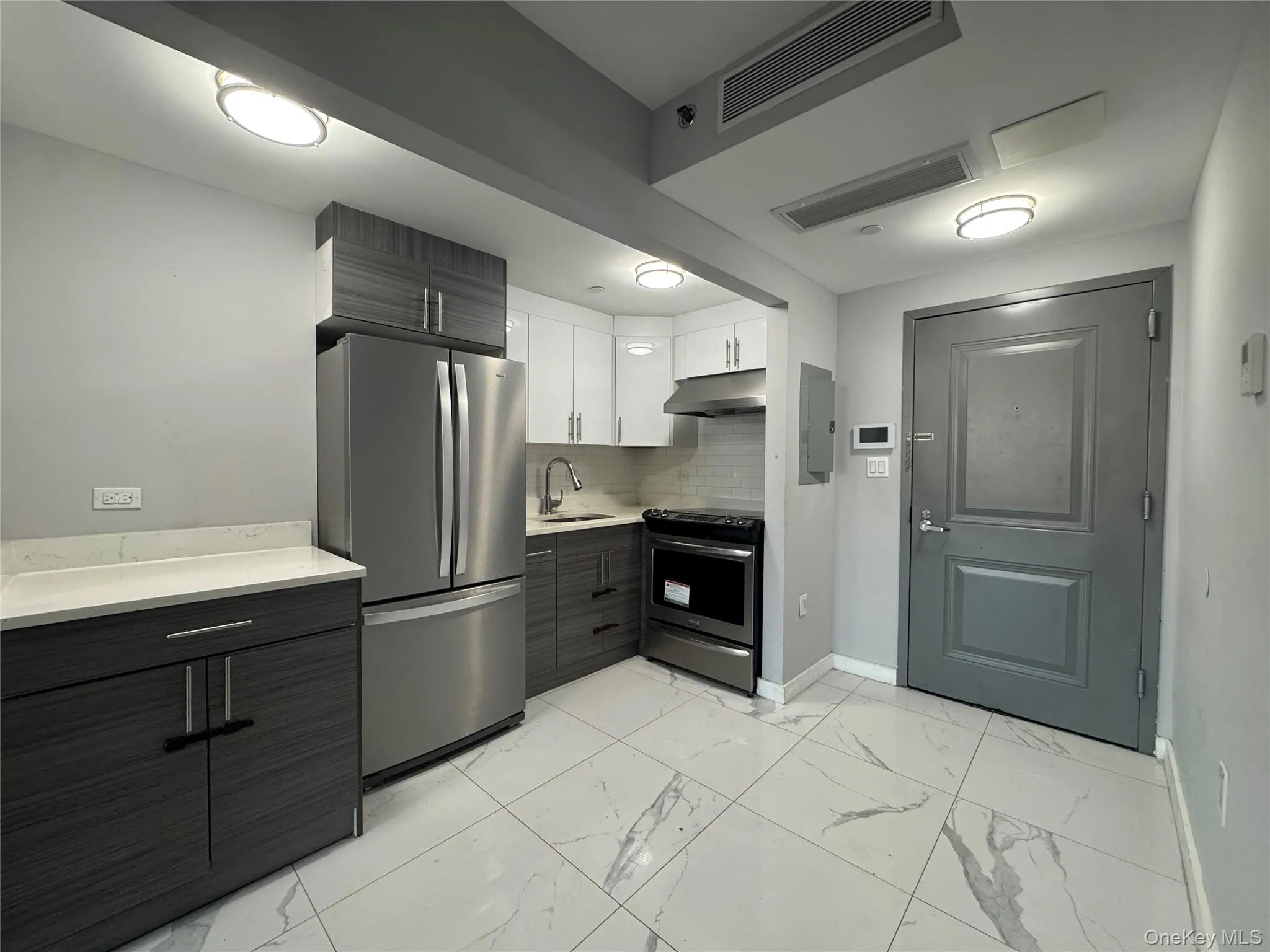 Kitchen with modern cabinets, stainless steel appliances, white cabinets, and light marble finish flooring Kitchen with modern cabinets, stainless steel appliances, white cabinets, and light marble finish flooring