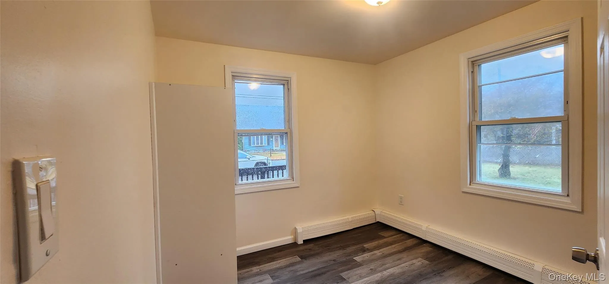 Empty room featuring dark wood-style floors, a baseboard radiator, and healthy amount of natural light Empty room featuring dark wood-style floors, a baseboard radiator, and healthy amount of natural light