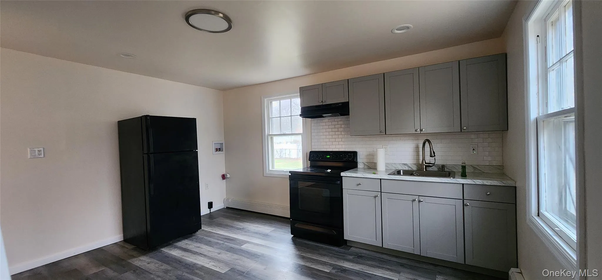 Kitchen with gray cabinets, light countertops, black appliances, and under cabinet range hood Kitchen with gray cabinets, light countertops, black appliances, and under cabinet range hood