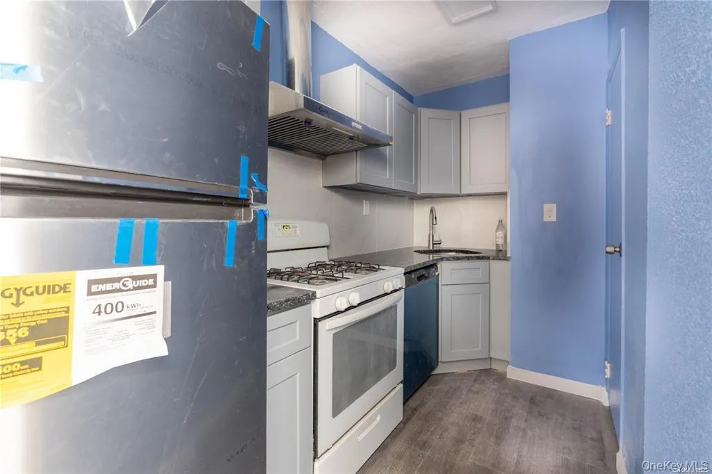 Kitchen featuring refrigerator, white gas range oven, dishwashing machine, dark wood-type flooring, and wall chimney range hood Kitchen featuring refrigerator, white gas range oven, dishwashing machine, dark wood-type flooring, and wall chimney range hood