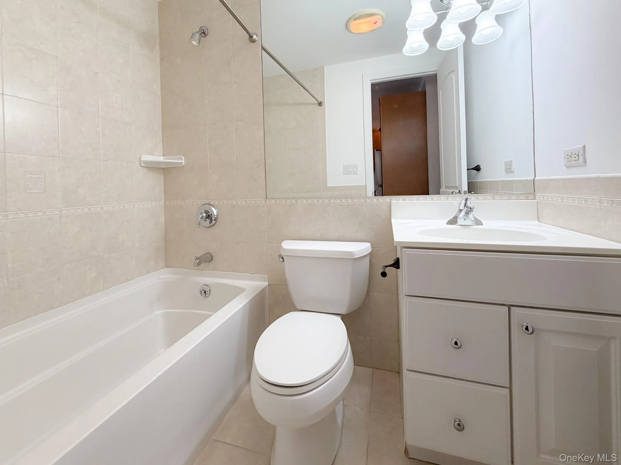Full bath featuring tile walls, vanity, shower / bath combination, and light tile patterned flooring Full bath featuring tile walls, vanity, shower / bath combination, and light tile patterned flooring