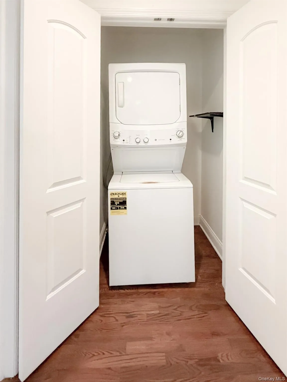 Laundry area with dark wood finished floors and stacked washing machine and dryer Laundry area with dark wood finished floors and stacked washing machine and dryer