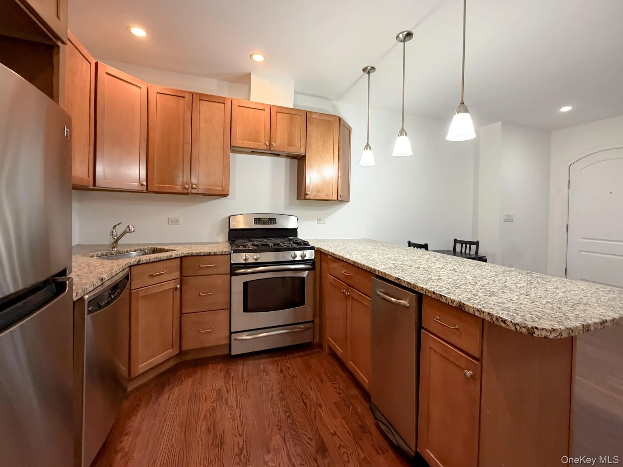 Kitchen featuring appliances with stainless steel finishes, light stone counters, recessed lighting, pendant lighting, and dark wood finished floors Kitchen featuring appliances with stainless steel finishes, light stone counters, recessed lighting, pendant lighting, and dark wood finished floors