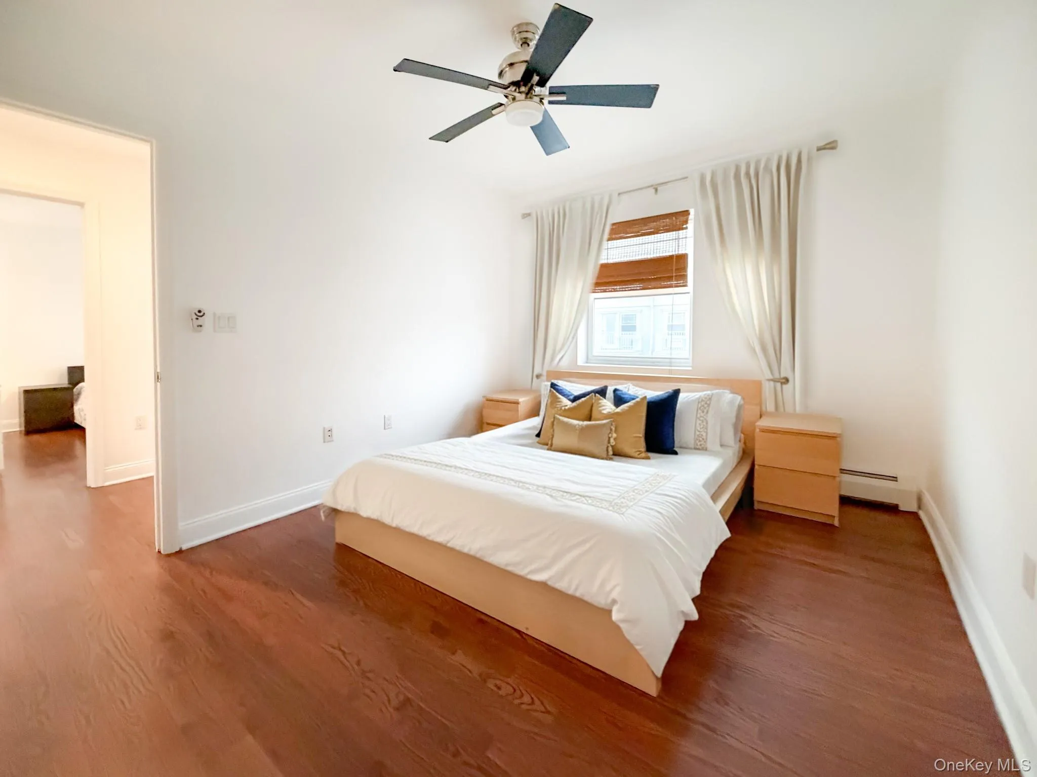 Bedroom with wood finished floors, a ceiling fan, and a baseboard heating unit Bedroom with wood finished floors, a ceiling fan, and a baseboard heating unit