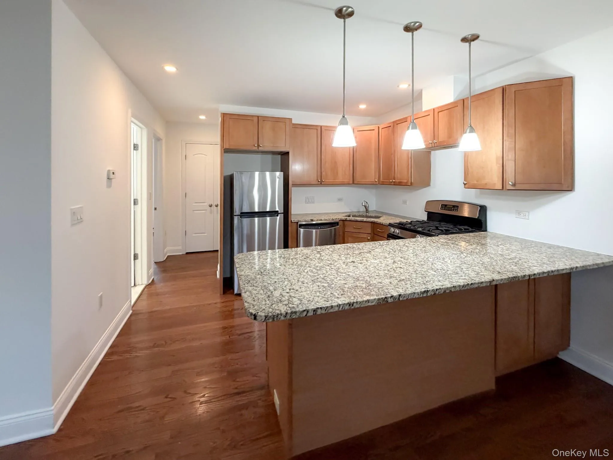 Kitchen featuring a peninsula, recessed lighting, appliances with stainless steel finishes, light stone countertops, and decorative light fixtures Kitchen featuring a peninsula, recessed lighting, appliances with stainless steel finishes, light stone countertops, and decorative light fixtures