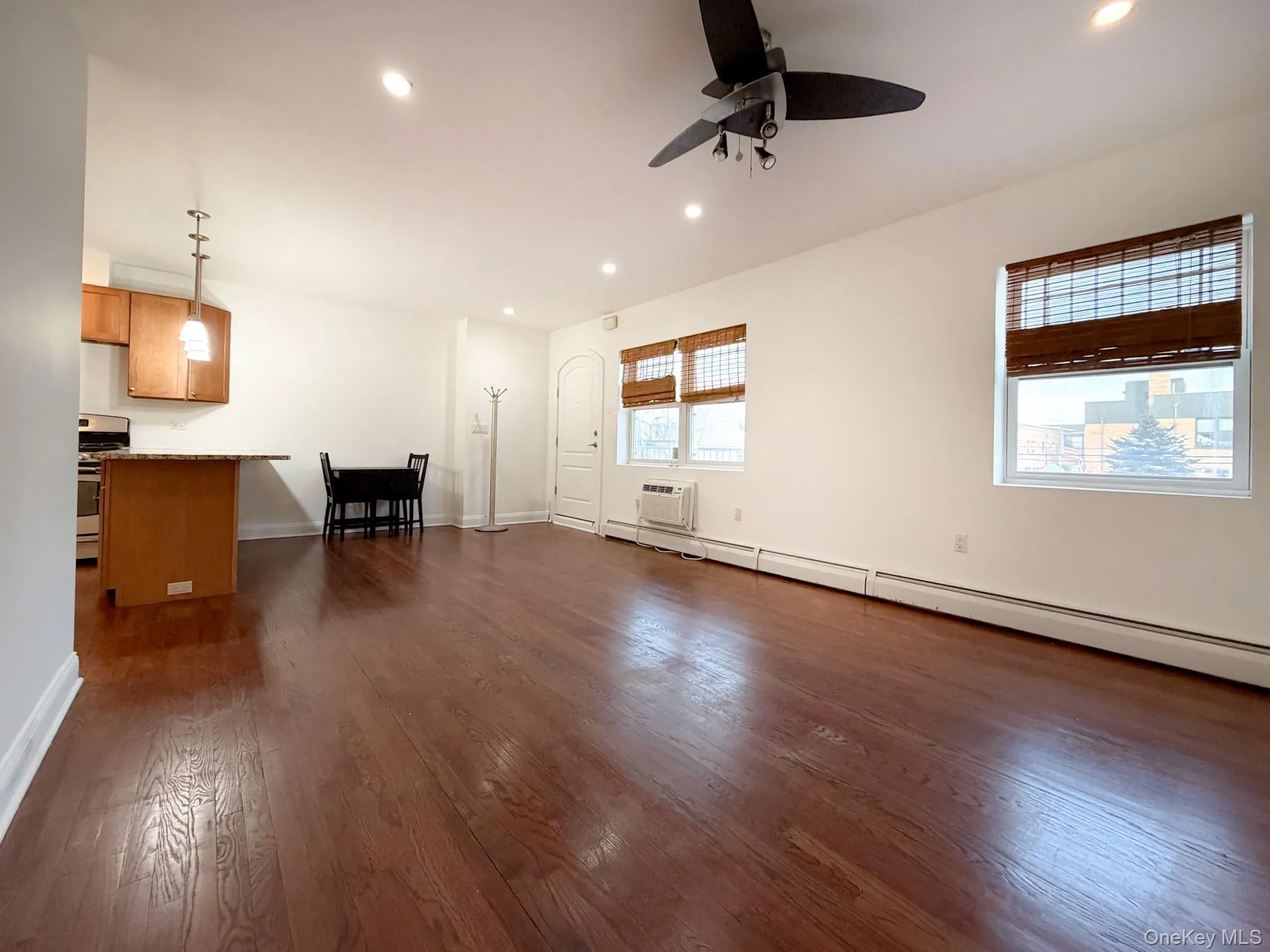 Unfurnished living room featuring a baseboard radiator, recessed lighting, dark wood finished floors, a ceiling fan, and a wall mounted air conditioner Unfurnished living room featuring a baseboard radiator, recessed lighting, dark wood finished floors, a ceiling fan, and a wall mounted air conditioner