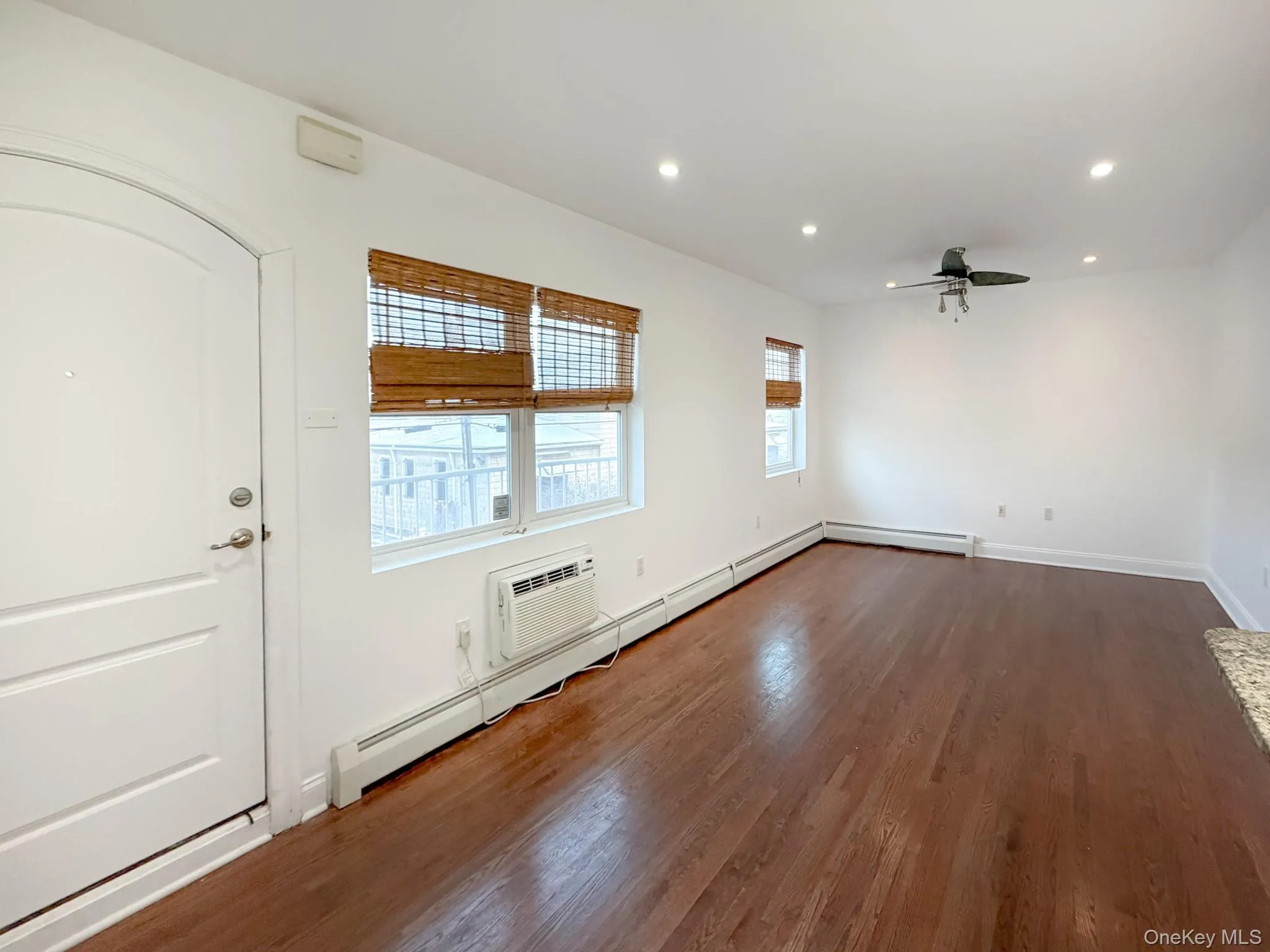 Spare room with recessed lighting, dark wood finished floors, ceiling fan, an AC wall unit, and a baseboard radiator Spare room with recessed lighting, dark wood finished floors, ceiling fan, an AC wall unit, and a baseboard radiator