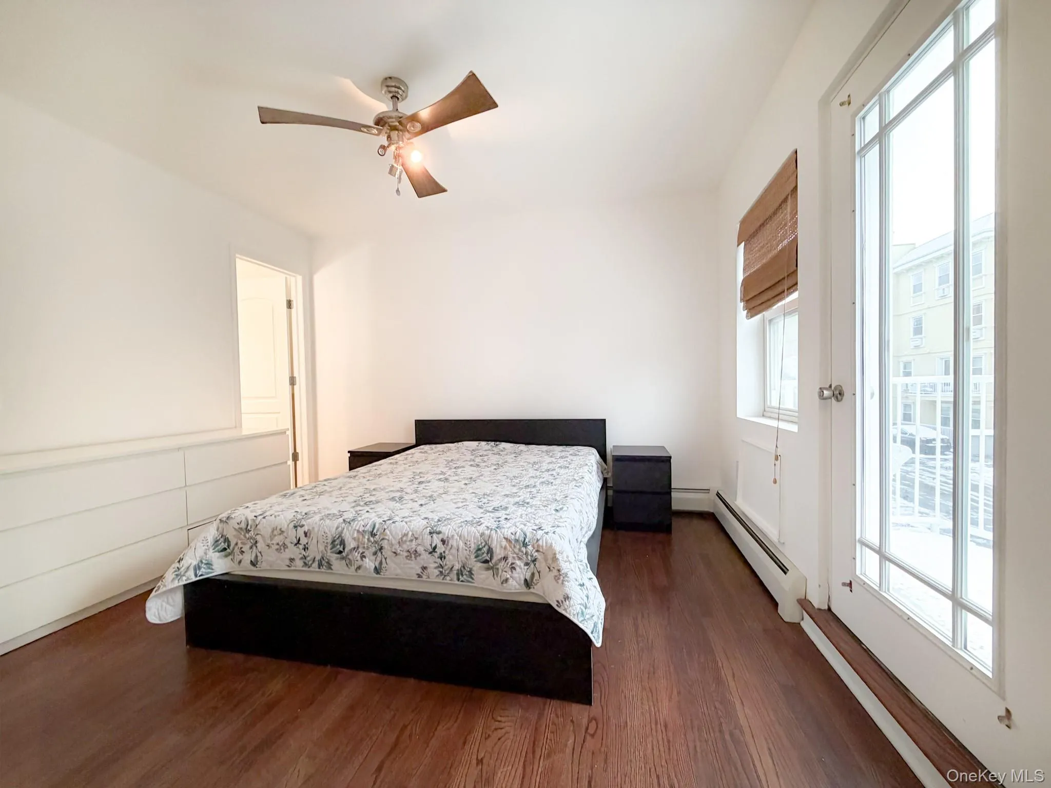 Bedroom with dark wood-style flooring, a ceiling fan, access to exterior, and baseboard heating Bedroom with dark wood-style flooring, a ceiling fan, access to exterior, and baseboard heating