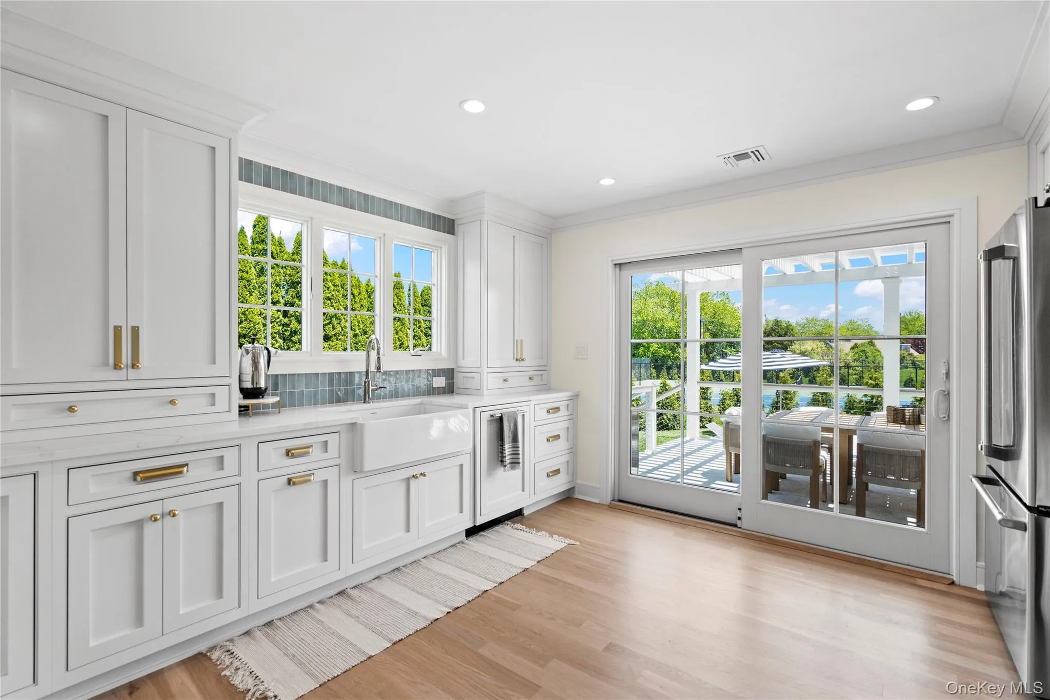 Kitchen with white cabinets, freestanding refrigerator, light stone counters, light wood-style flooring, and tasteful backsplash Kitchen with white cabinets, freestanding refrigerator, light stone counters, light wood-style flooring, and tasteful backsplash
