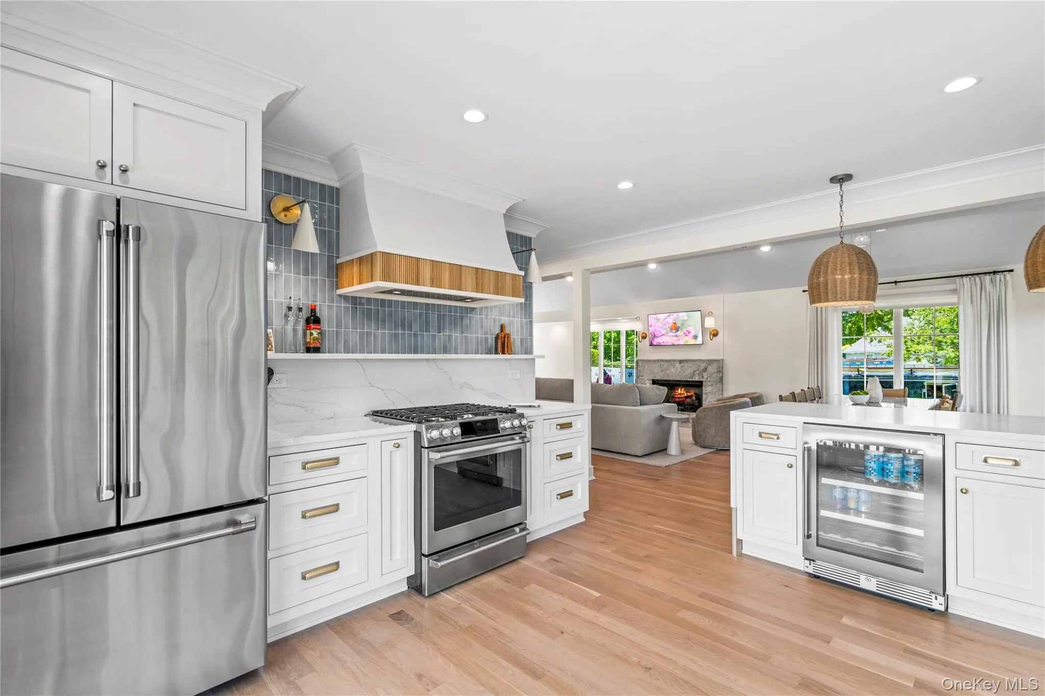 Kitchen featuring stainless steel appliances, white cabinets, open floor plan, a warm lit fireplace, and ornamental molding Kitchen featuring stainless steel appliances, white cabinets, open floor plan, a warm lit fireplace, and ornamental molding