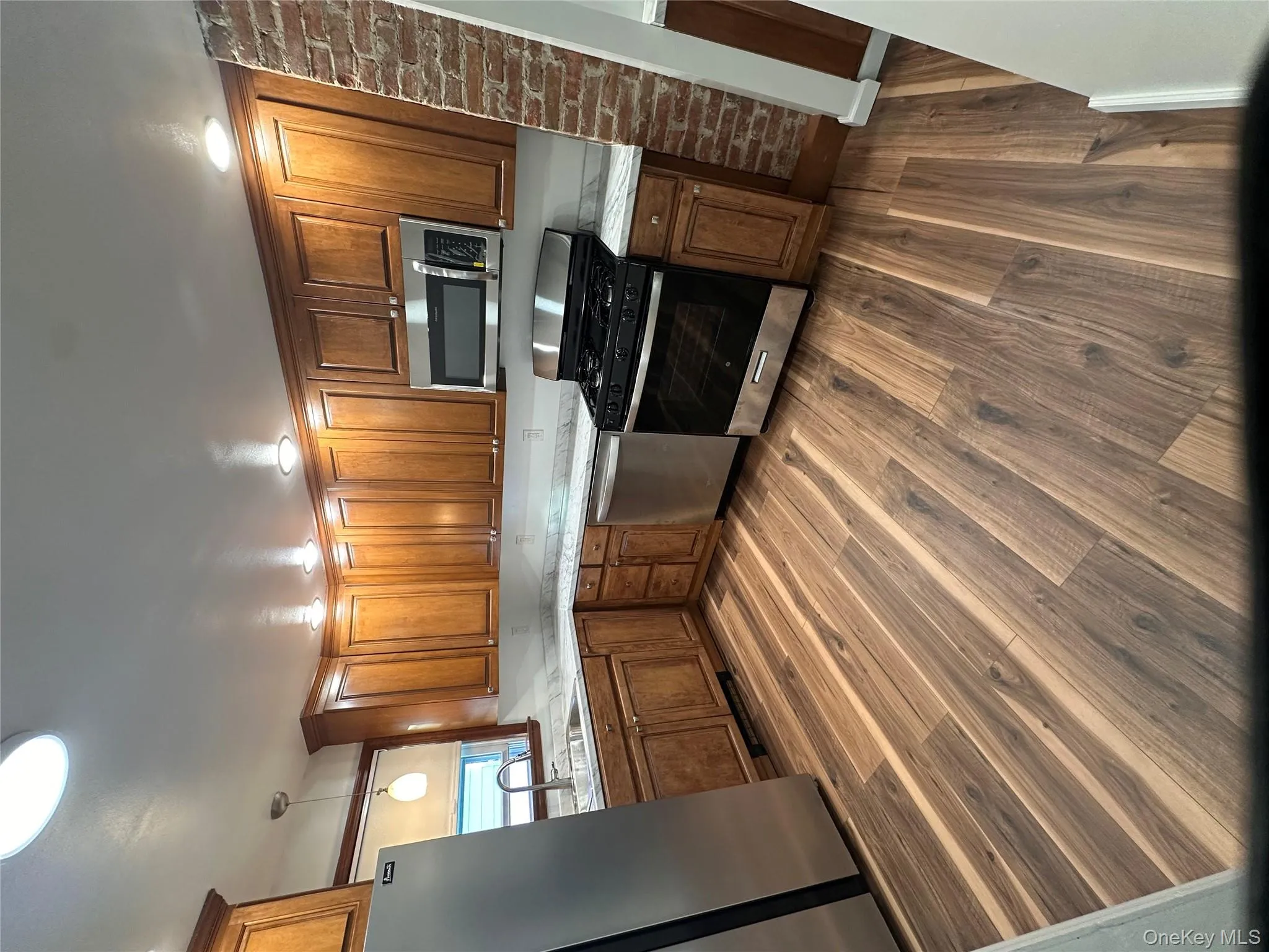 Kitchen featuring appliances with stainless steel finishes, brown cabinetry, dark wood finished floors, and light stone countertops Kitchen featuring appliances with stainless steel finishes, brown cabinetry, dark wood finished floors, and light stone countertops