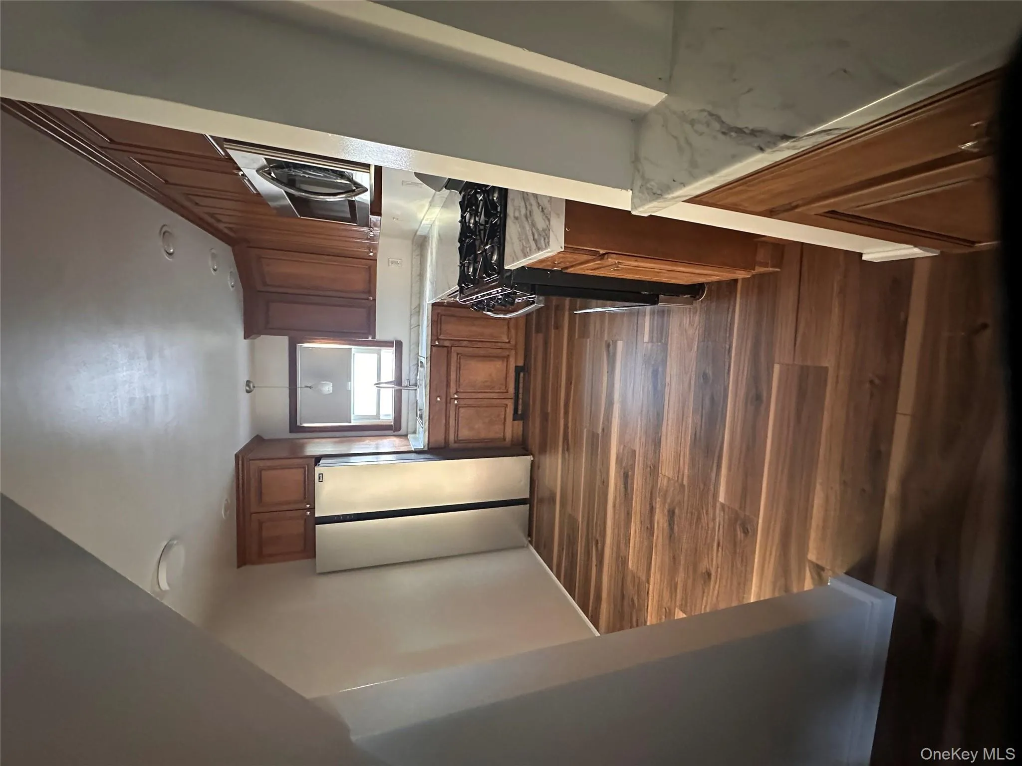 Kitchen featuring brown cabinetry, range, stainless steel fridge, dark wood-style floors, and decorative light fixtures Kitchen featuring brown cabinetry, range, stainless steel fridge, dark wood-style floors, and decorative light fixtures